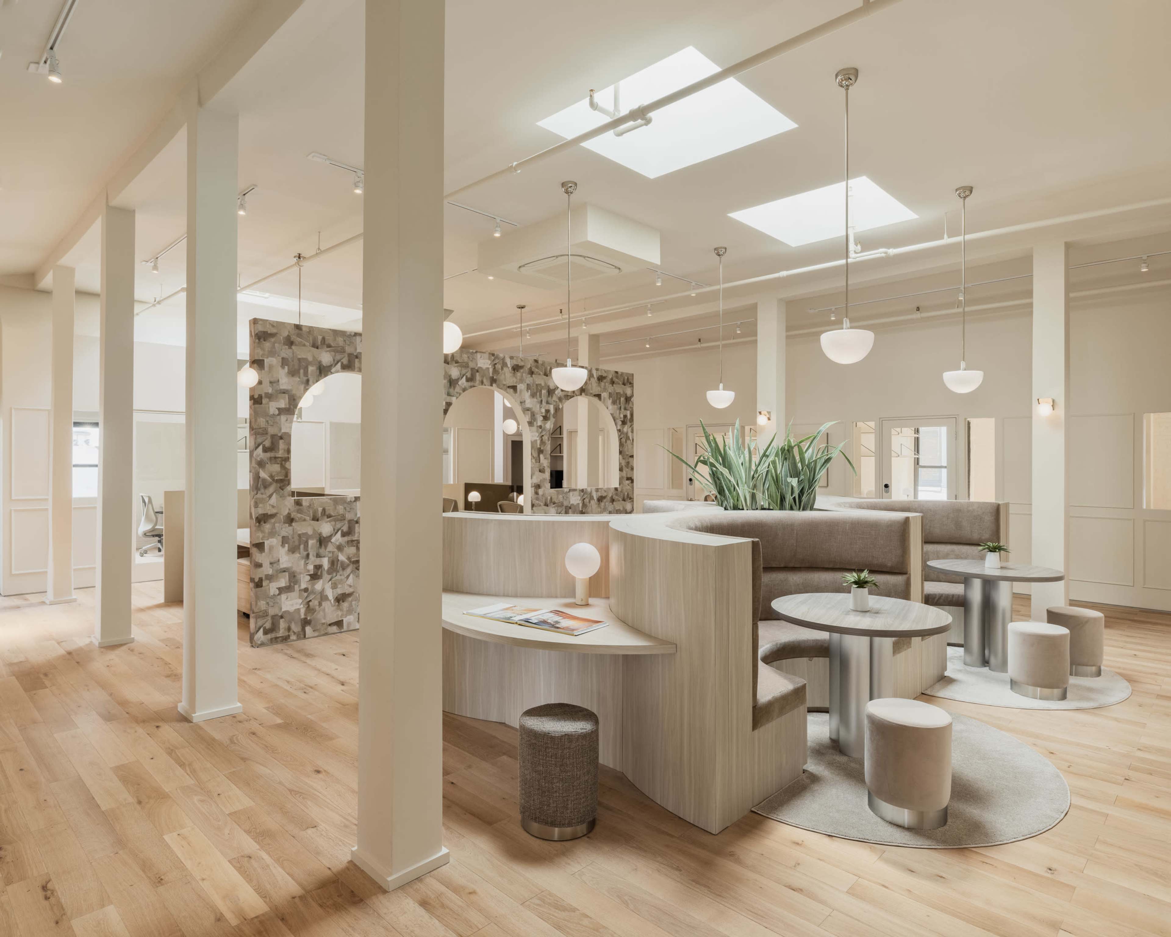 A spacious, modern interior with light wooden flooring, circular light fixtures, and various seating areas separated by decorative partitions.