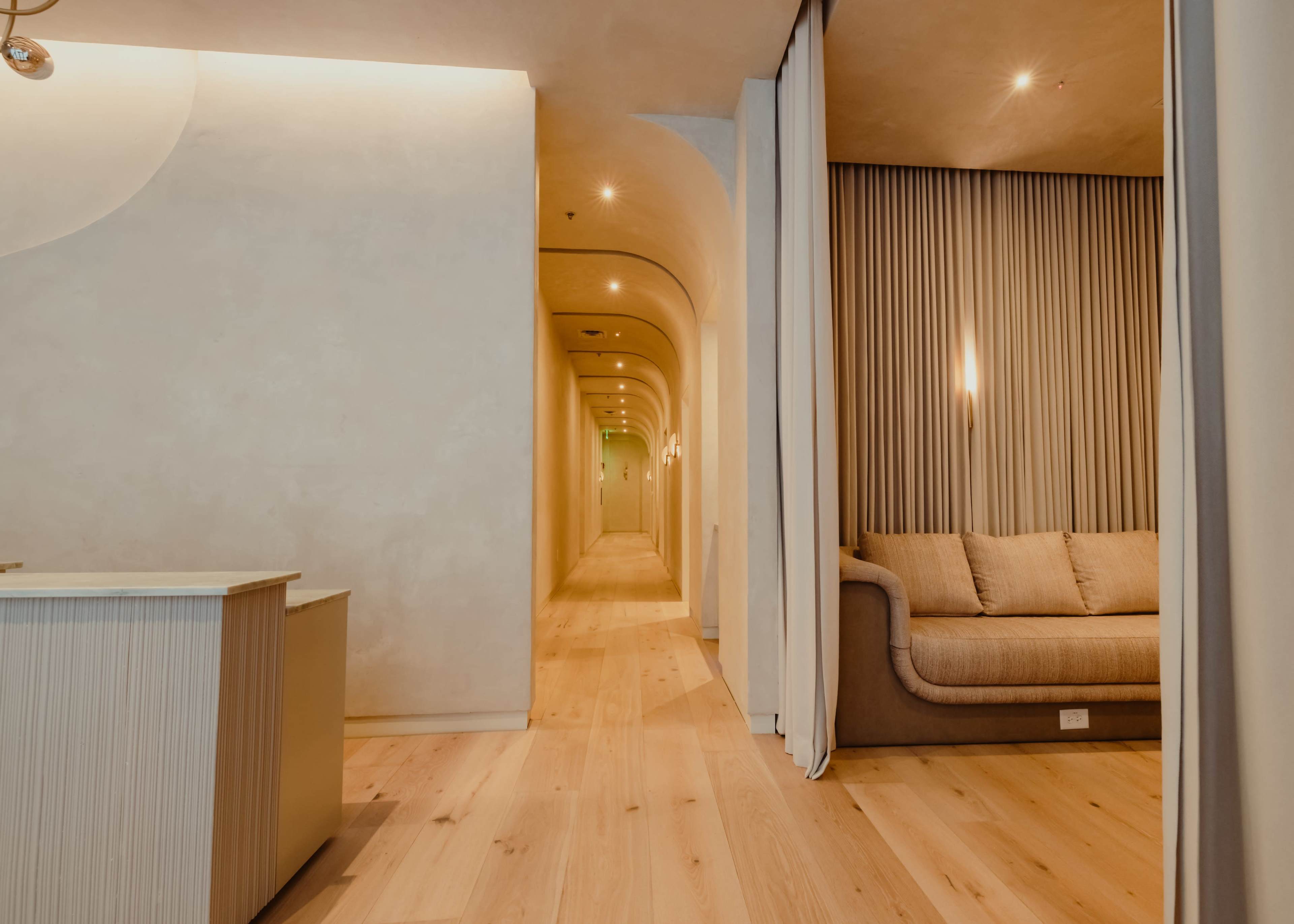 The image shows a well-lit hallway with a seating area and softly curved walls.