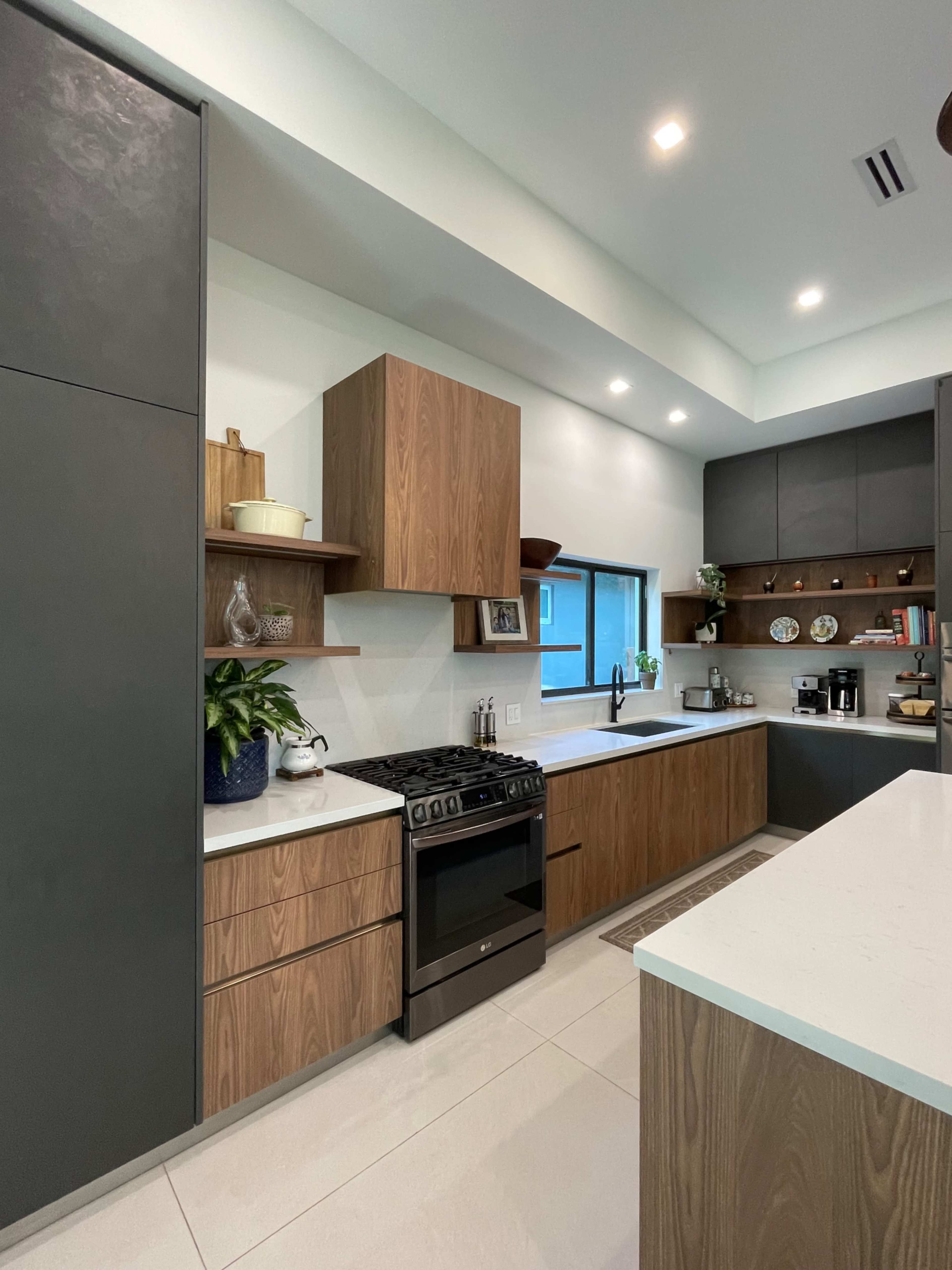 The image shows a modern kitchen featuring a combination of dark cabinetry and light wooden elements, with a gas stove, countertop, and various decorative items on open shelves.