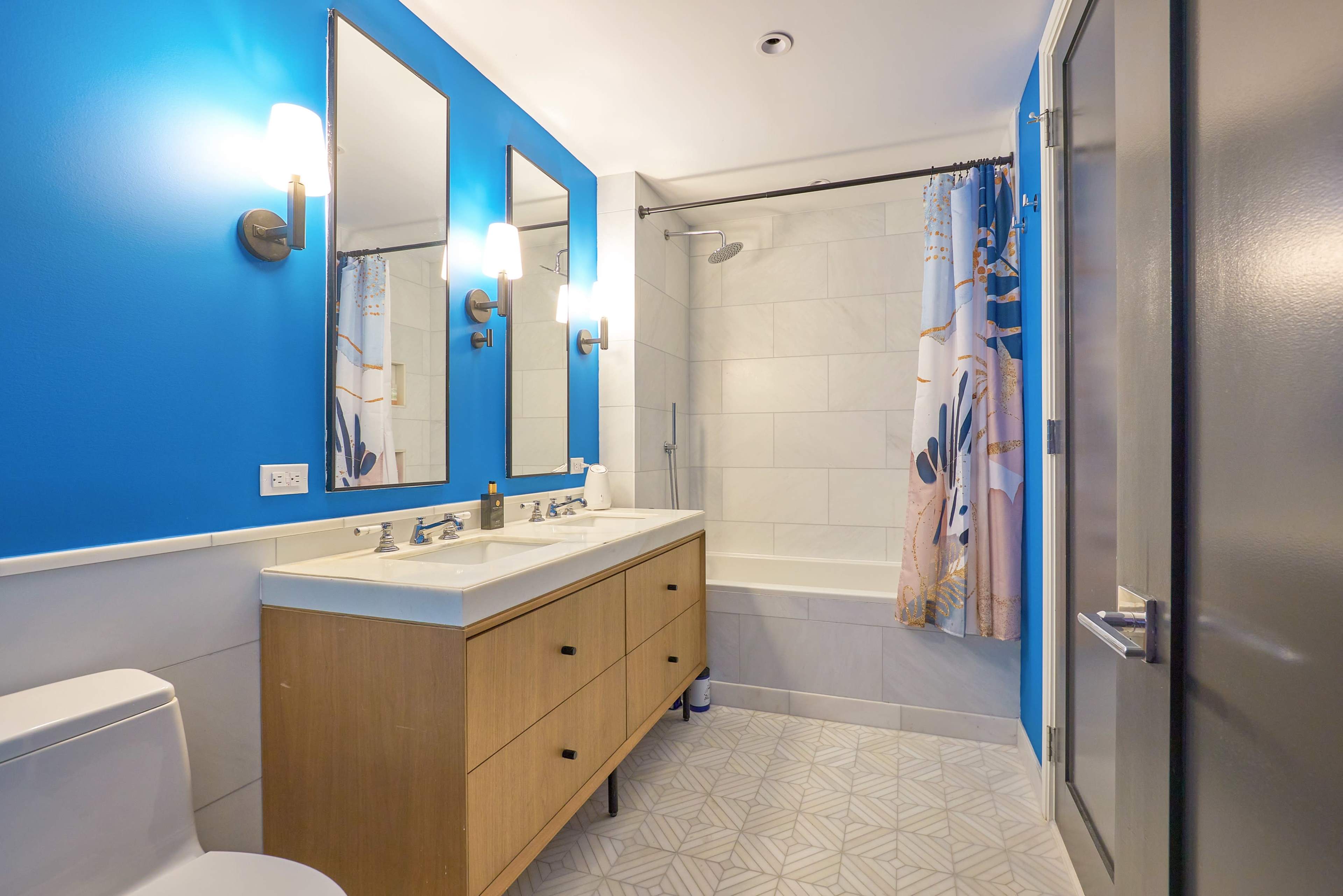 A modern bathroom with two sinks, a bathtub, a blue accent wall, and a patterned shower curtain.