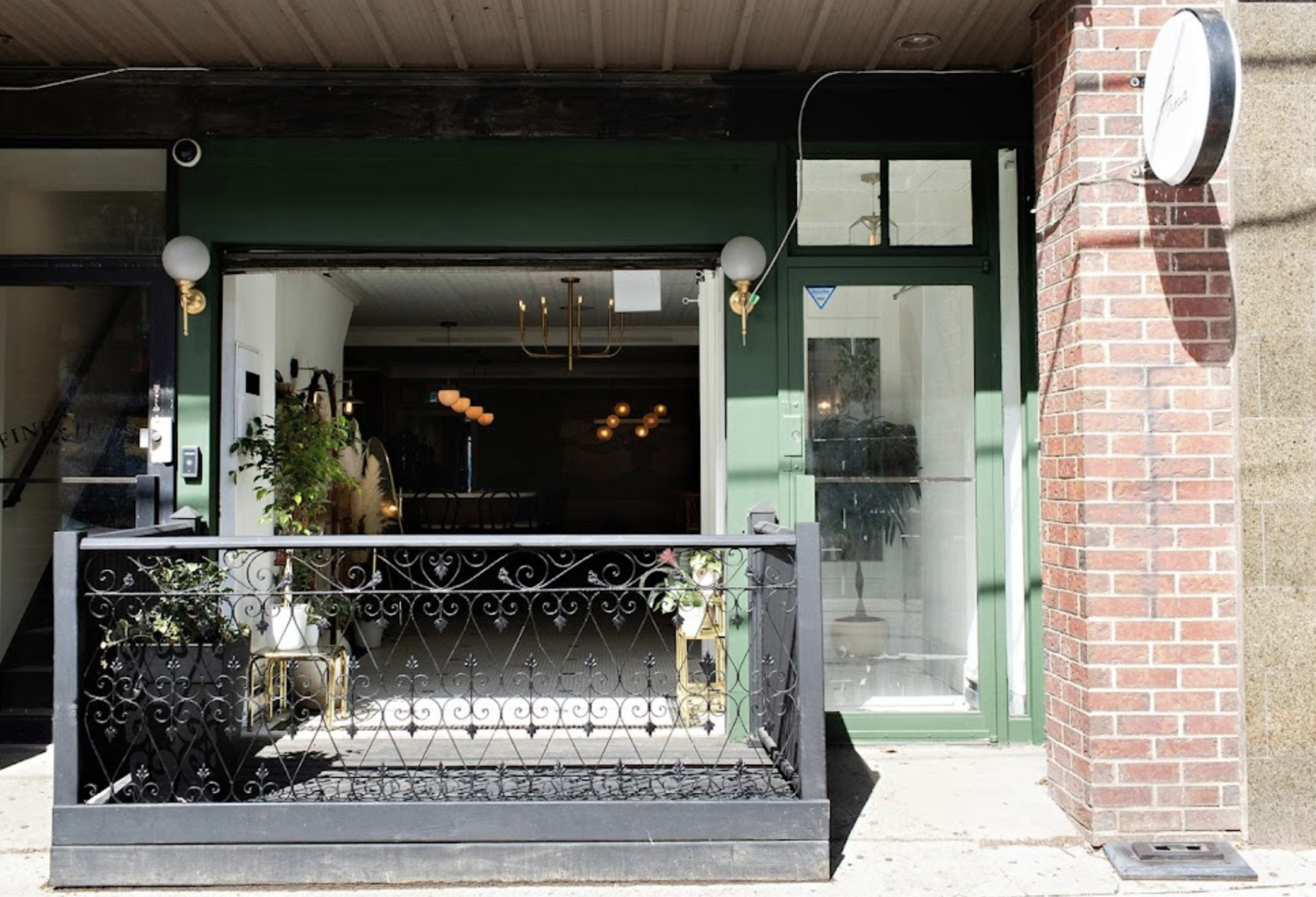 The exterior of a storefront with a decorative wrought-iron railing and large windows displaying a dimly lit interior.