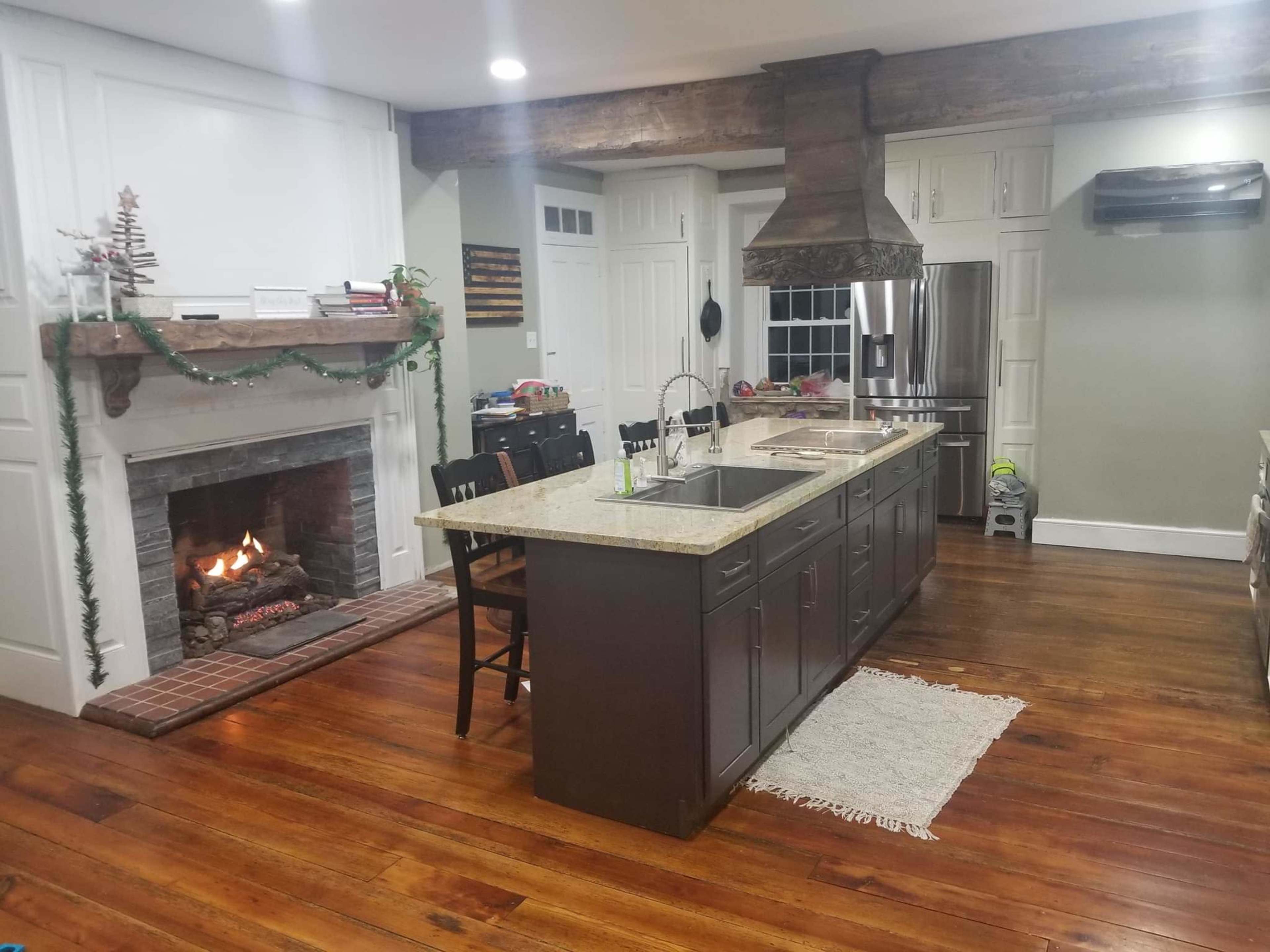 The kitchen features an island with dark cabinetry, a large hood over the stovetop, and a fireplace to the side, all set on polished wood flooring.