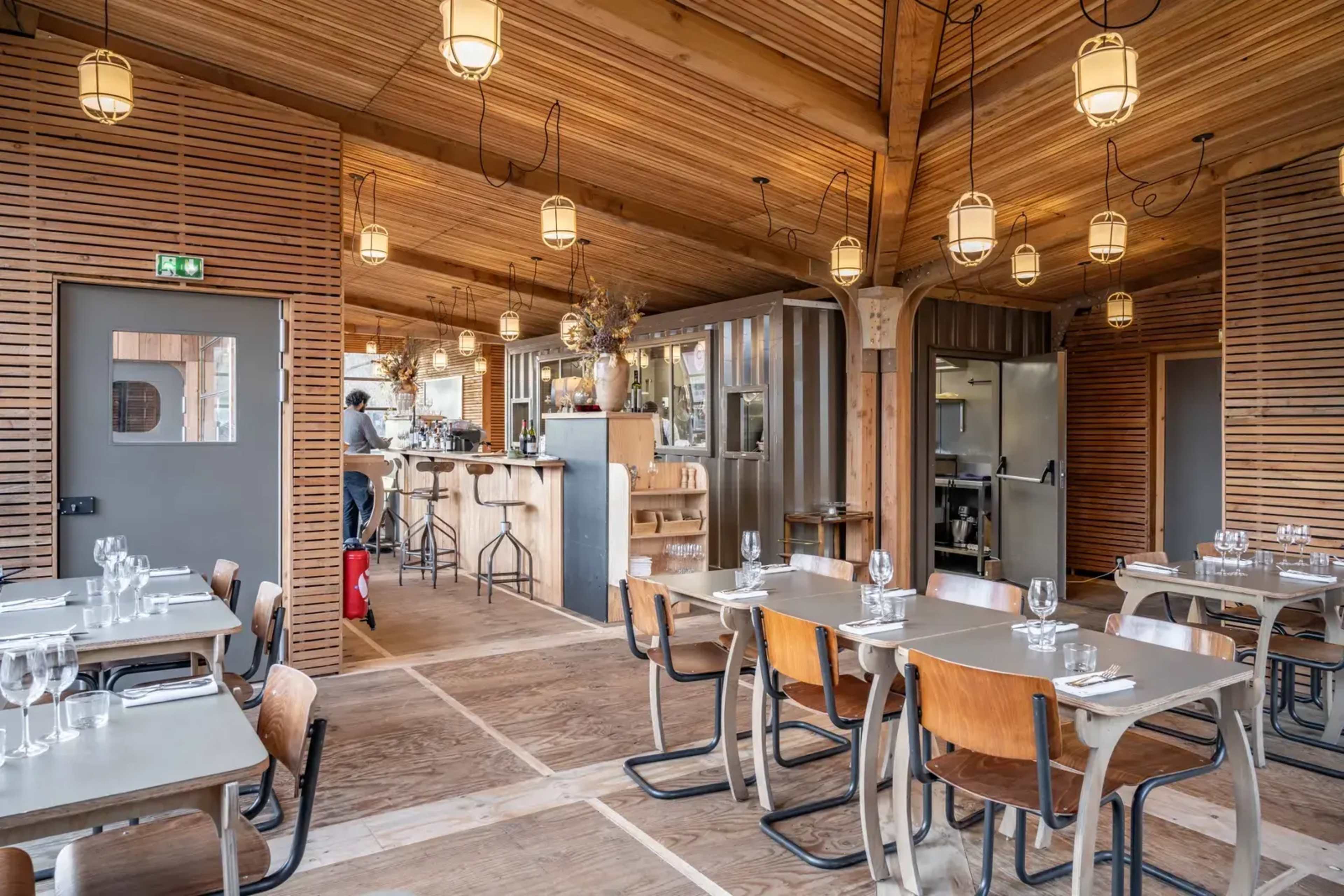 The interior of a restaurant featuring wooden beams, pendant lighting, and tables set for dining.