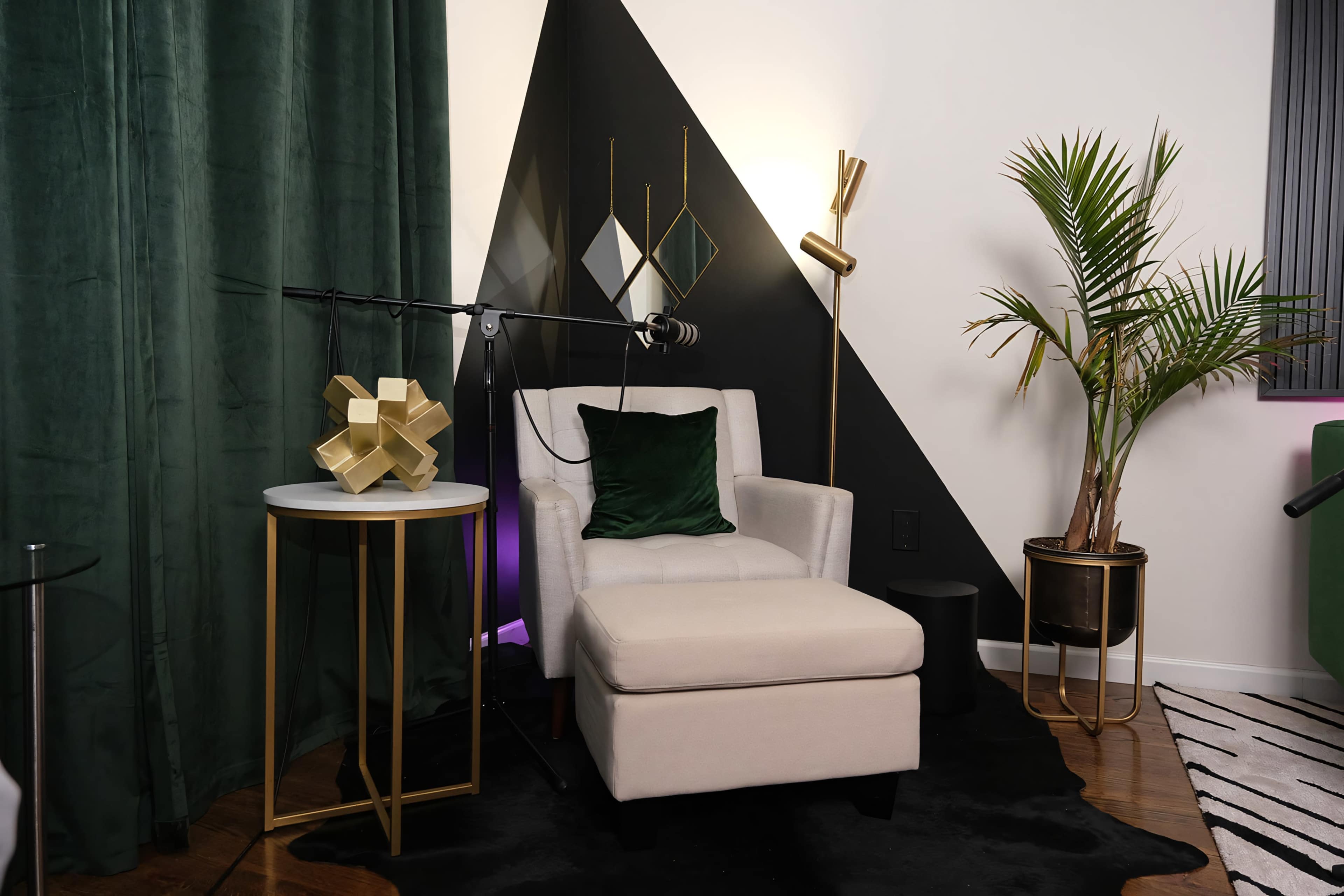 A modern seating area with a white armchair, a decorative gold sculpture on a small table, a potted palm, and a black and green geometric wall design.