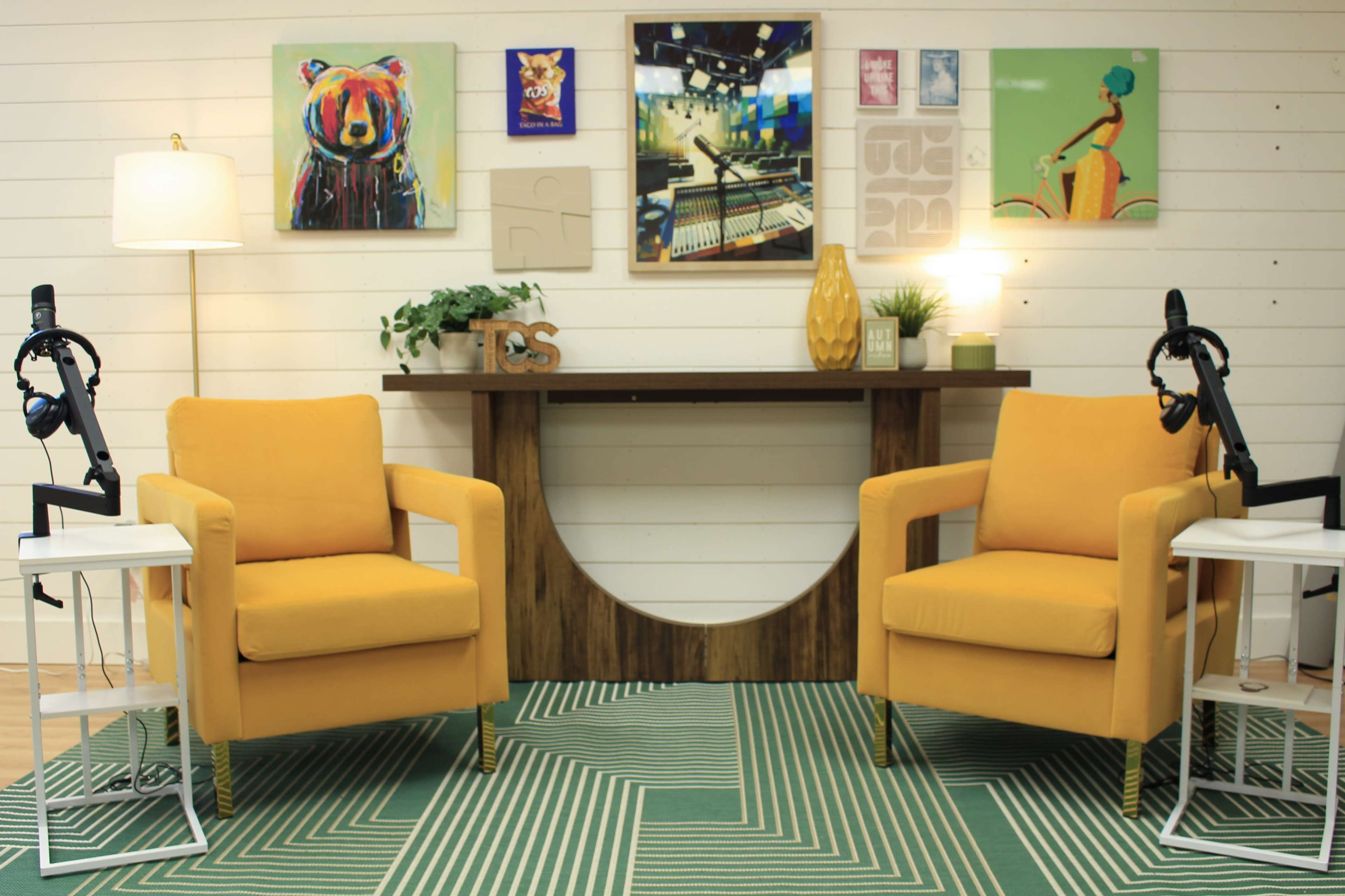 A cozy room with two yellow armchairs facing each other, a wooden console table behind them, and several pieces of colorful artwork on the walls.