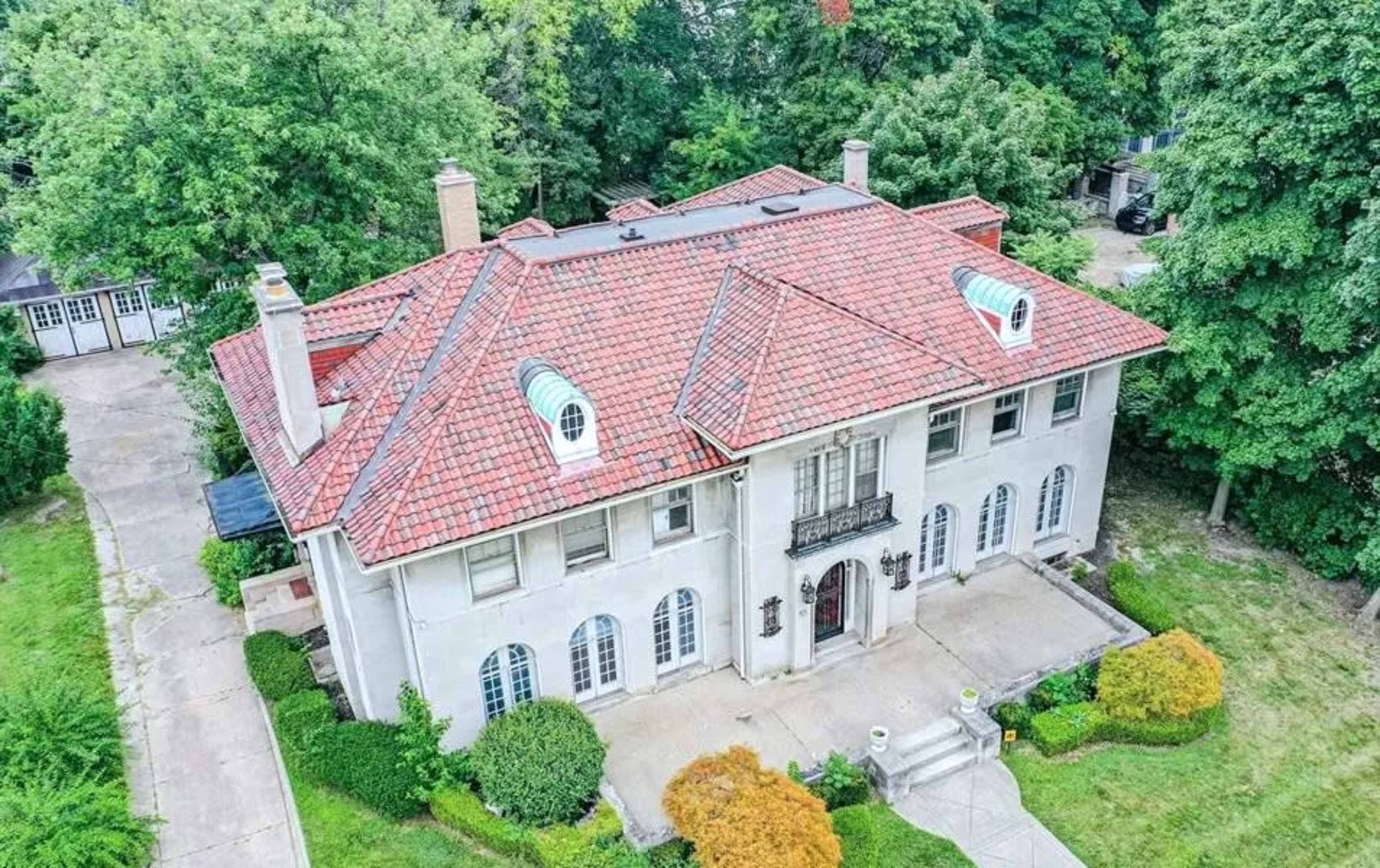 A large, two-story house with a red tiled roof, surrounded by greenery and a landscaped yard.