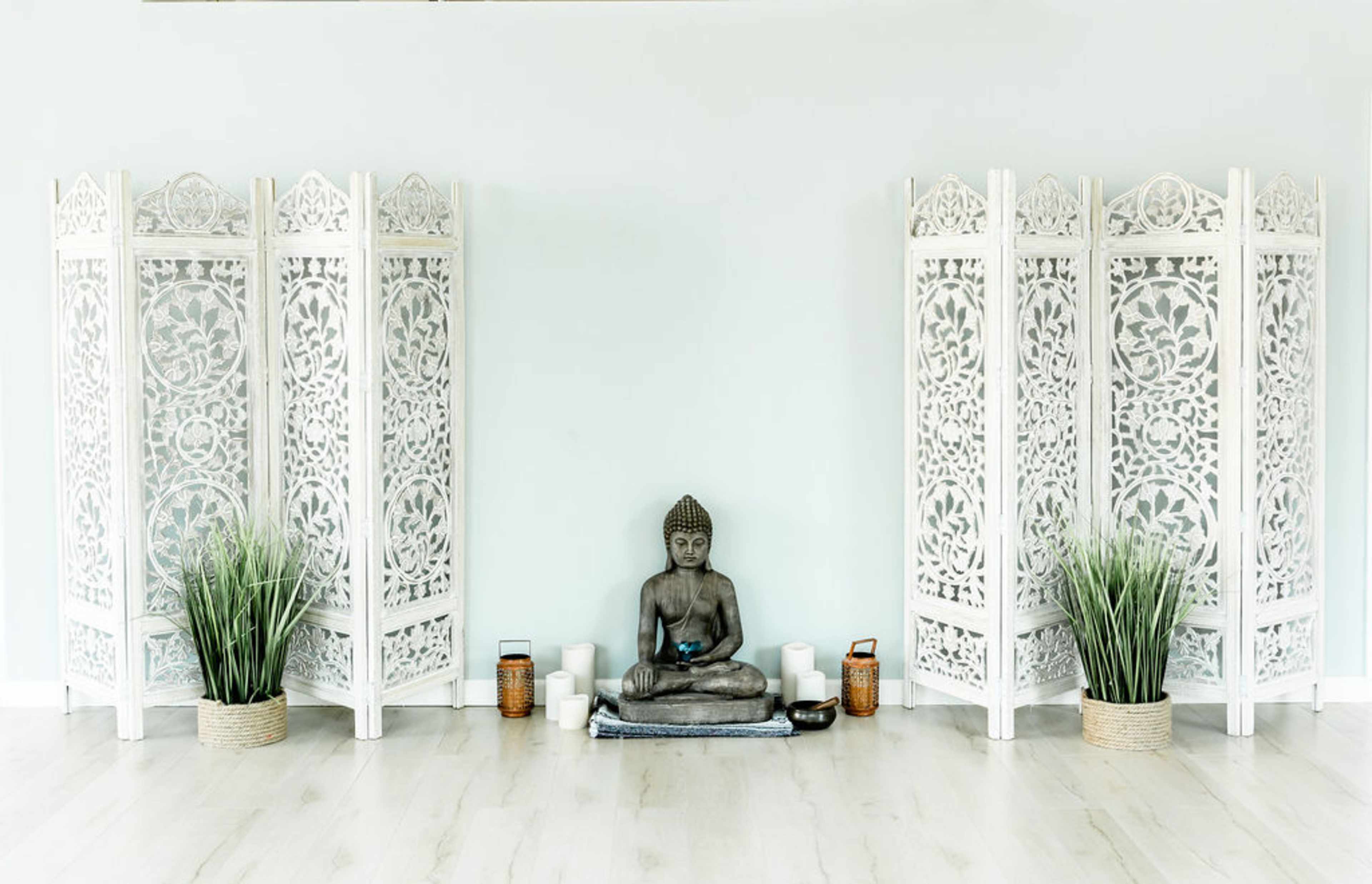 A serene interior space featuring a seated Buddha statue surrounded by ornamental room dividers and green plants.