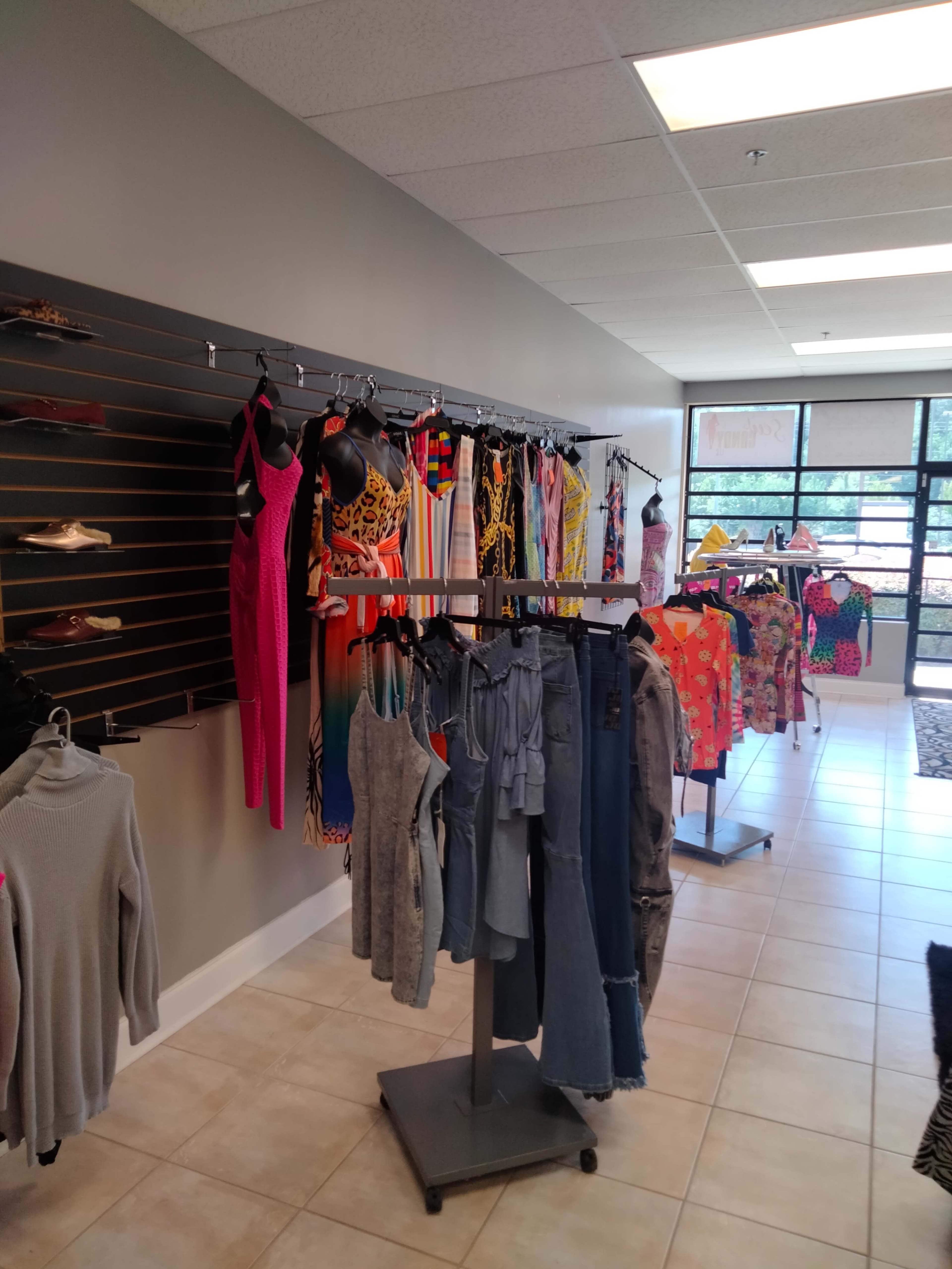 A clothing store displays a variety of colorful dresses and tops on hangers along a wall and on clothing racks.