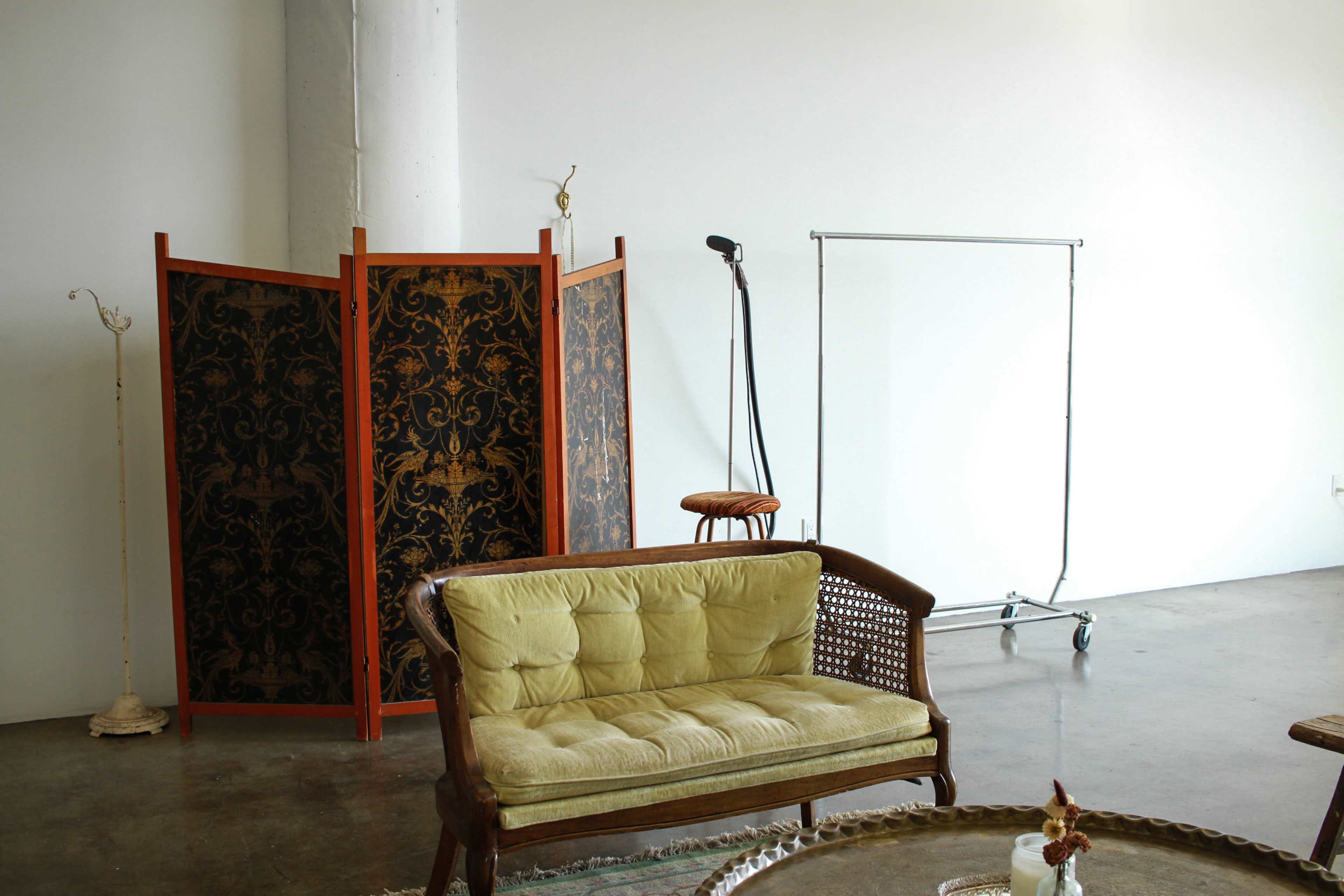 A minimalistic interior featuring a yellow couch, a decorative folding screen, a tall microphone stand, and a clothing rack against a plain background.