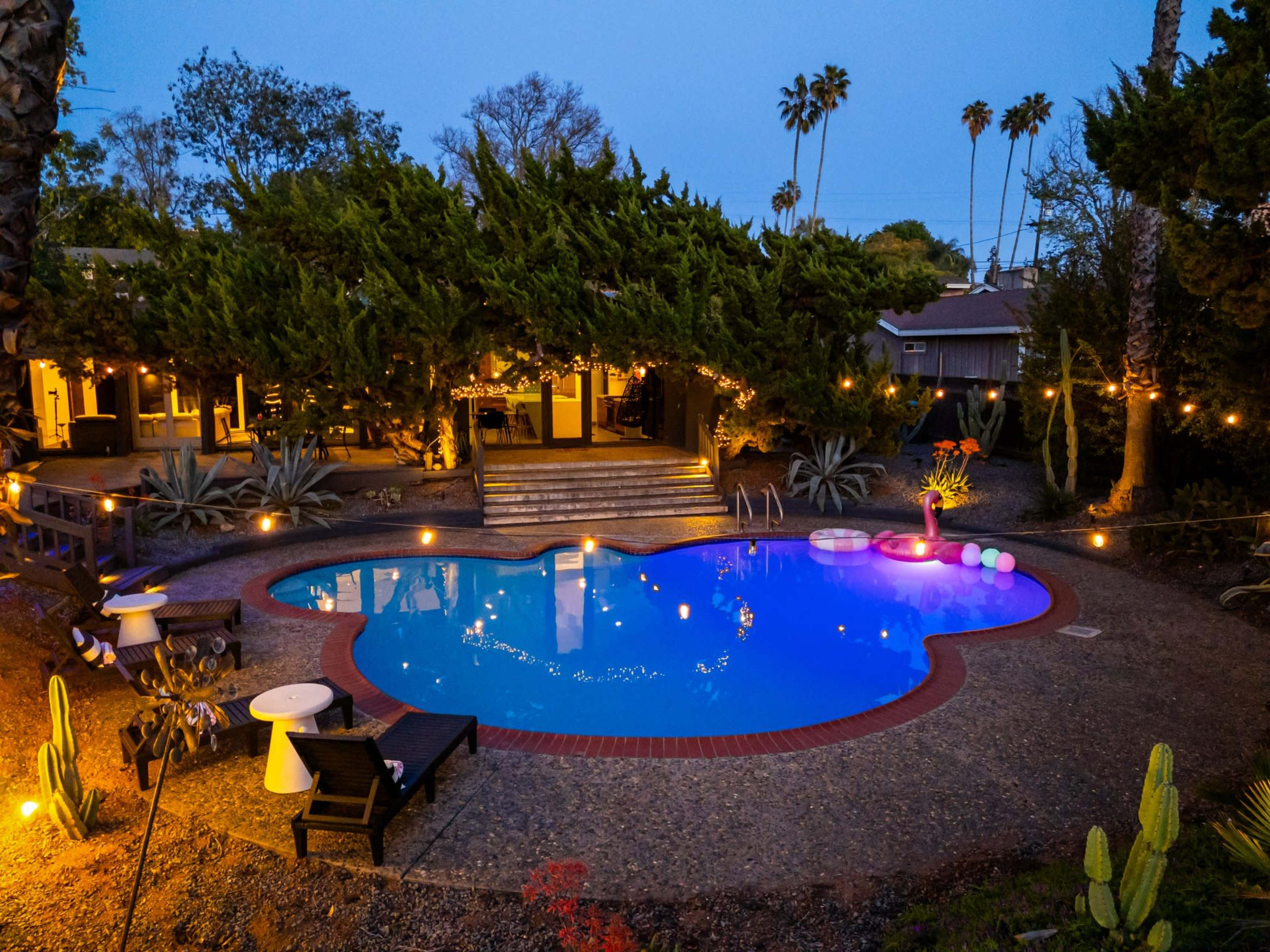 The image shows a heart-shaped pool surrounded by lush greenery and illuminated by string lights at dusk.