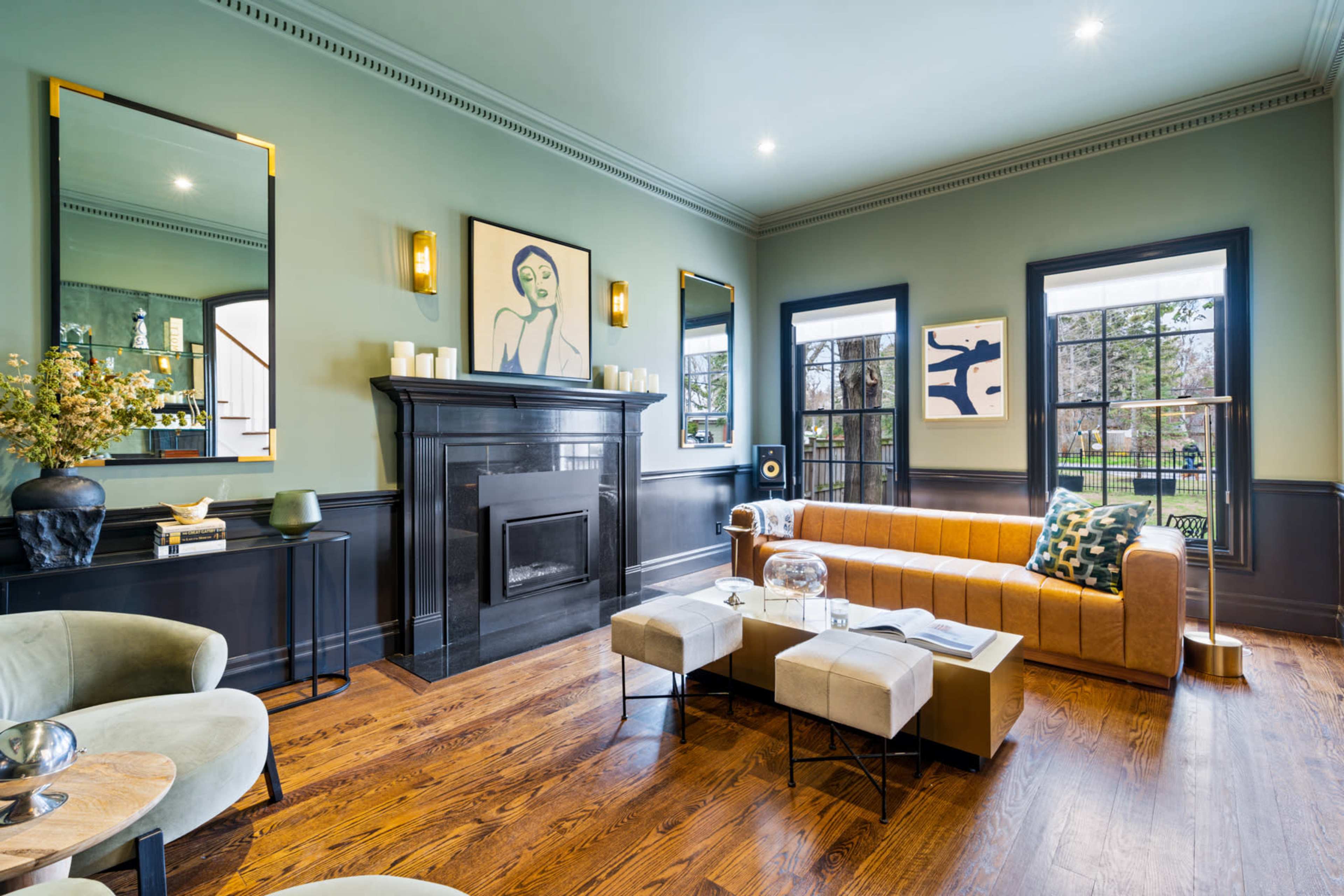 A modern living room with a tan leather sofa, a marble coffee table, and two mirrors on the walls, featuring artwork and large windows that overlook an outdoor view.