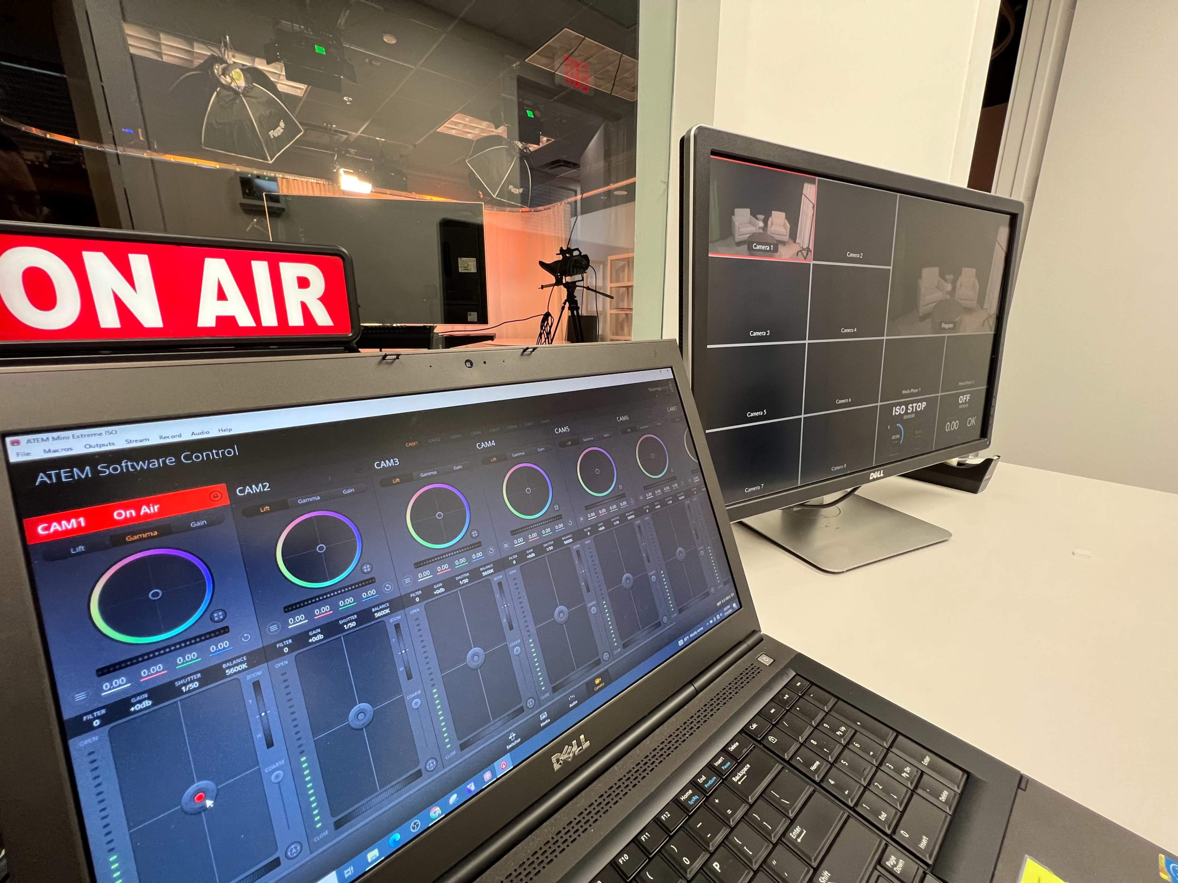 A laptop displaying the ATEM Software Control interface is positioned next to a monitor showing multiple camera feeds in a broadcasting studio with an "ON AIR" sign visible in the background.