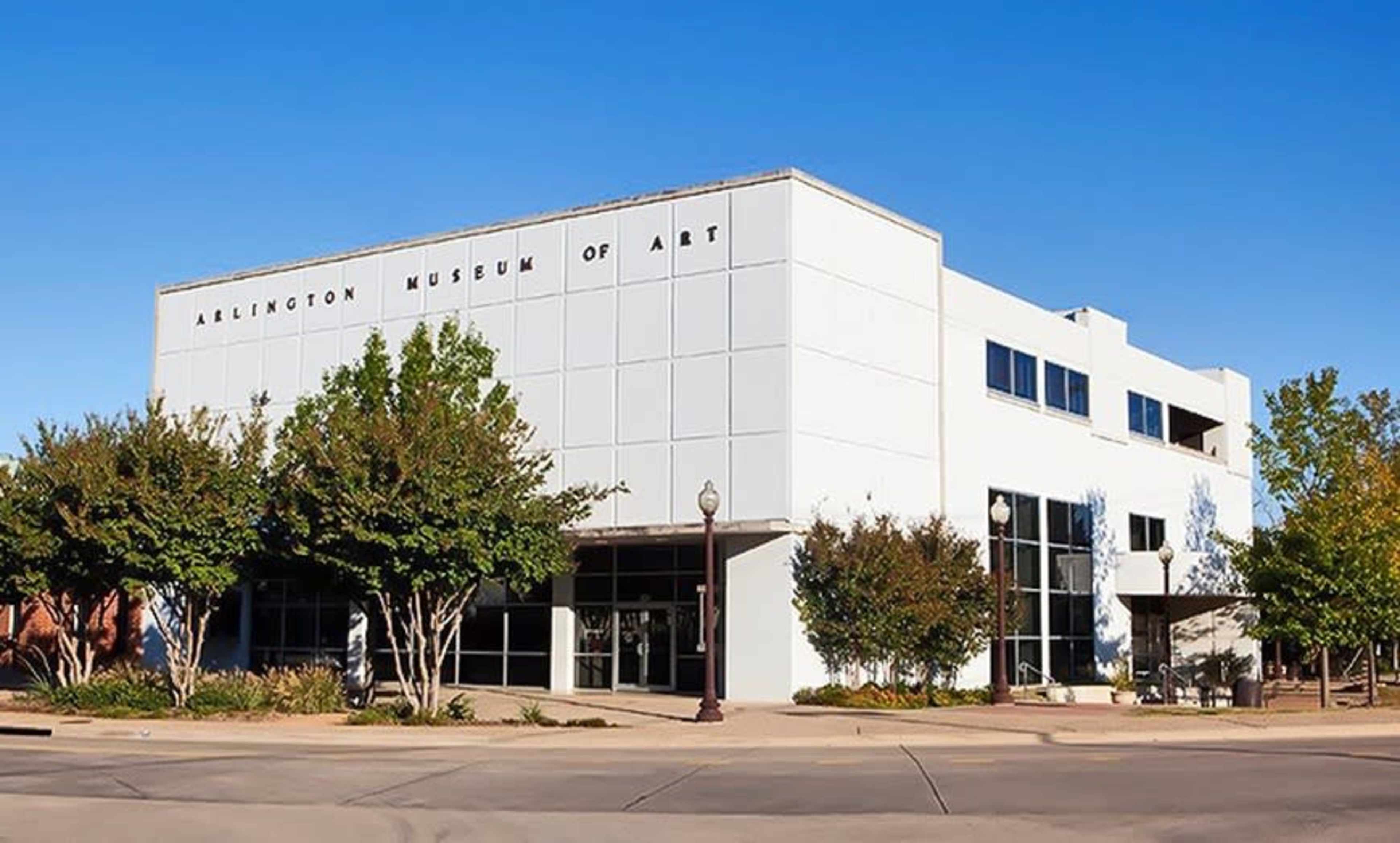 The Arlington Museum of Art features a modern white facade surrounded by well-maintained landscaping and clear blue skies.