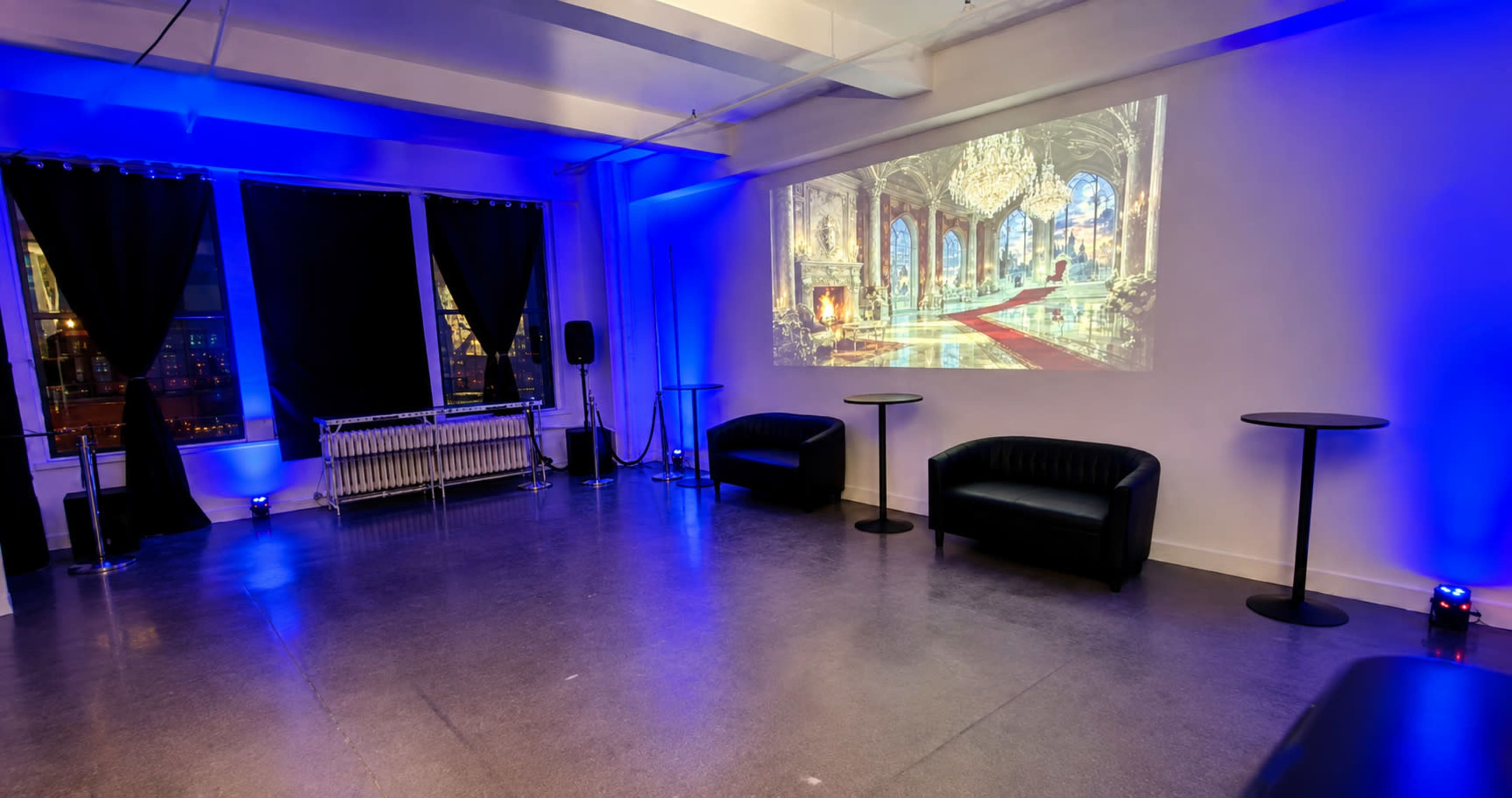 A modern event space features black leather couches, high tables, and blue lighting, with a decorative projection on the wall.