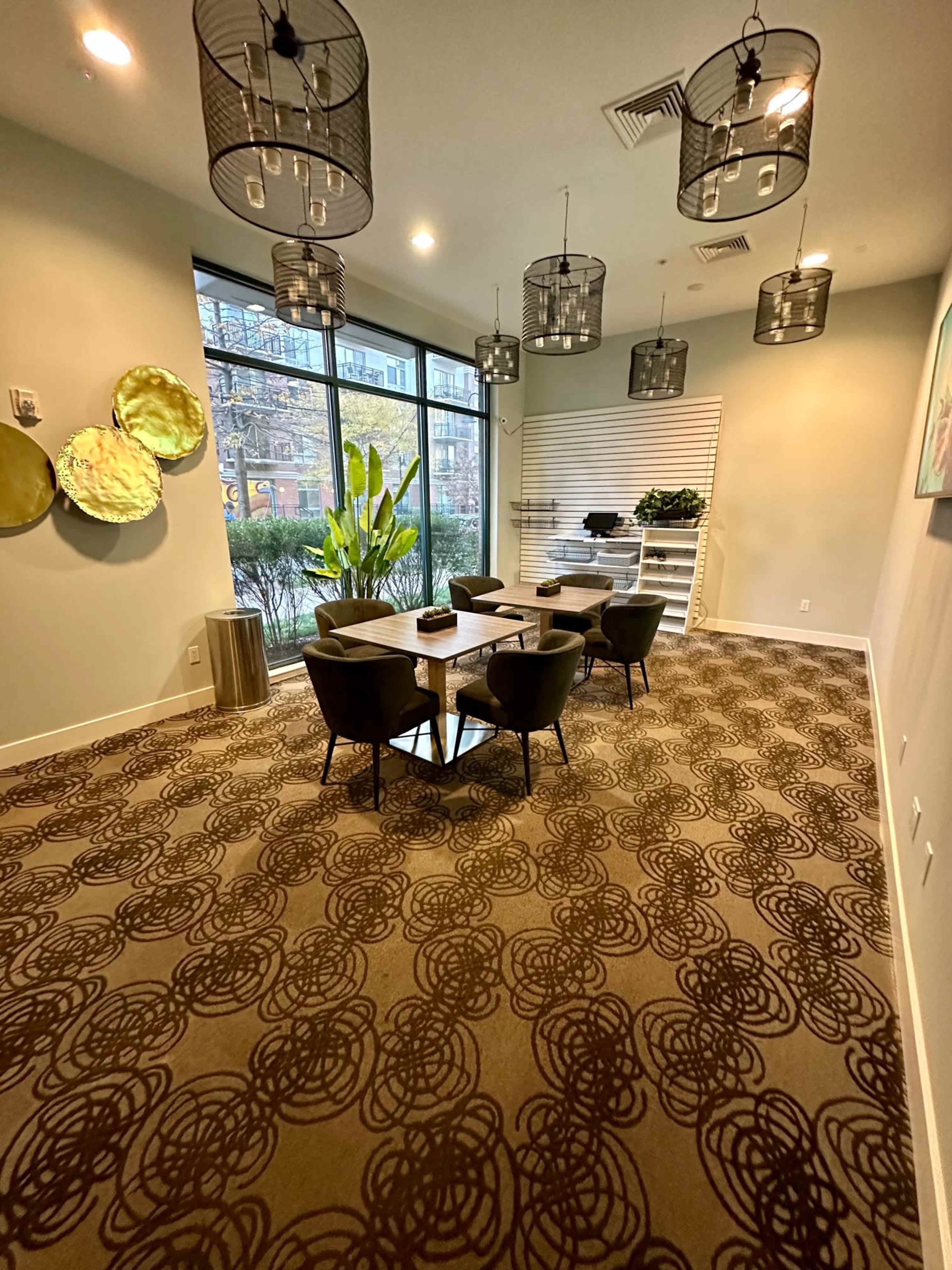 A modern meeting room features a large table surrounded by chairs, with pendant lights overhead and large windows showcasing a view of greenery outside.