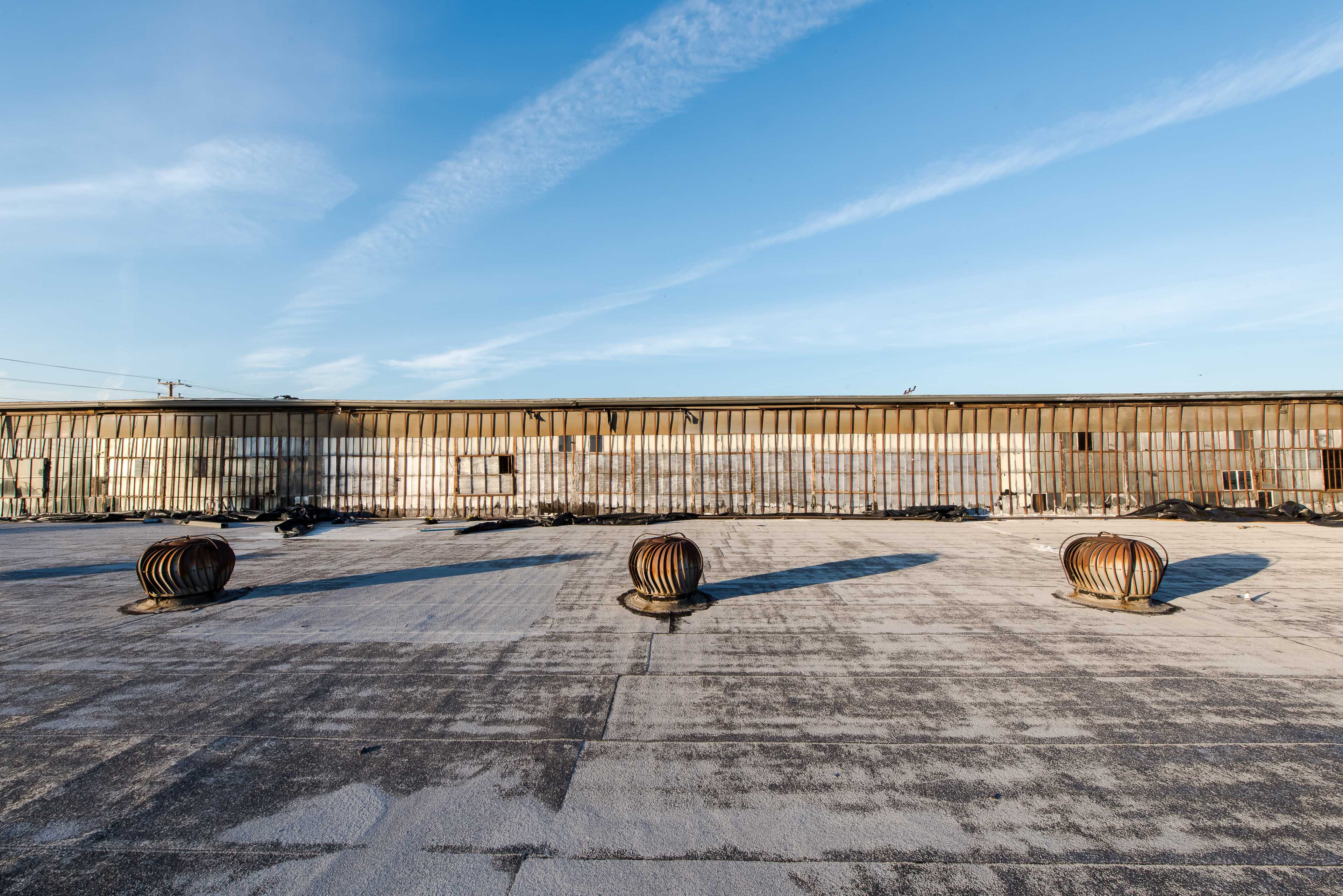 The image shows a rooftop with several round vents casting long shadows on a flat surface beneath a clear blue sky.
