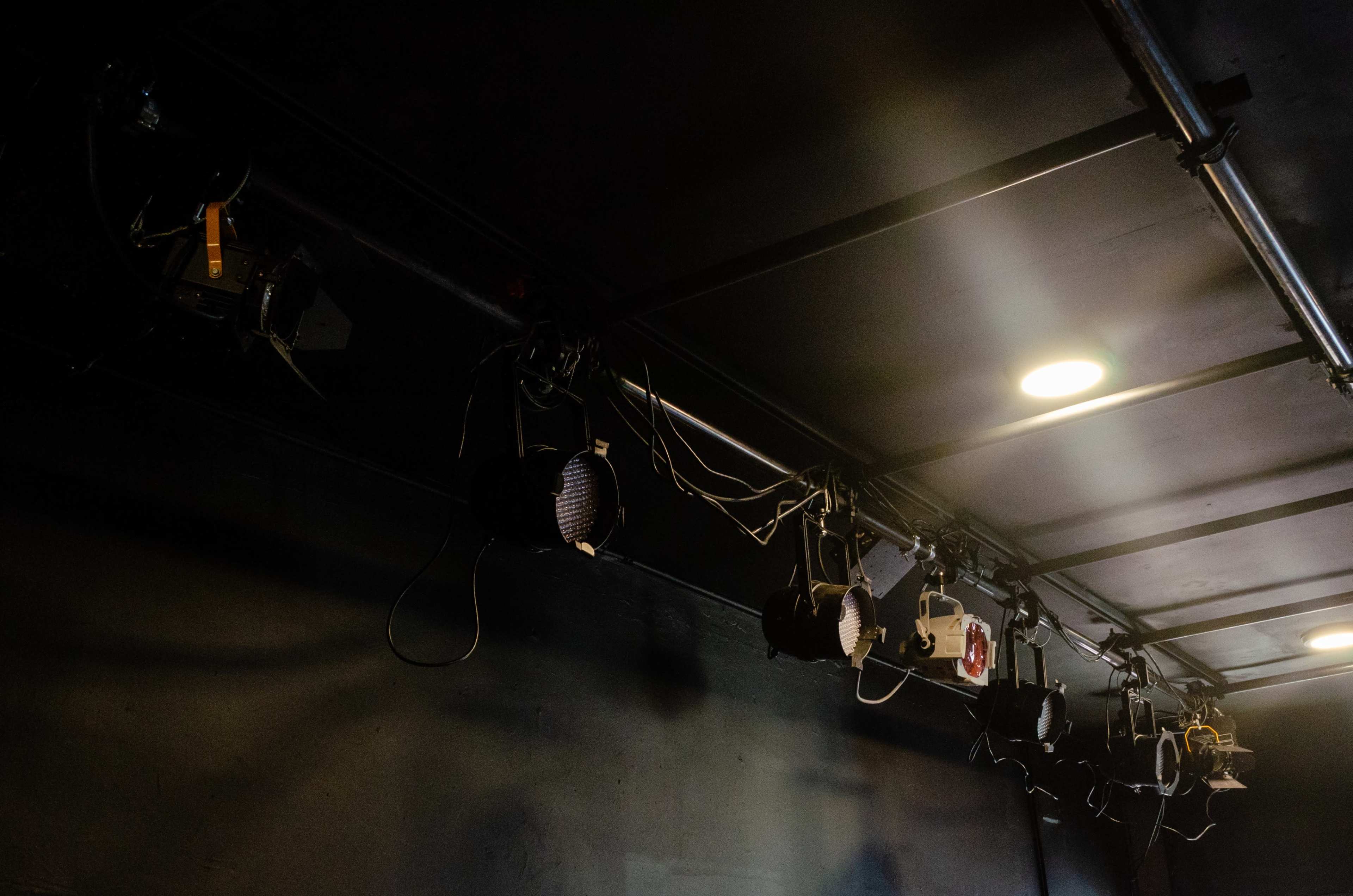 A row of stage lights mounted on a ceiling grid in a darkened room.