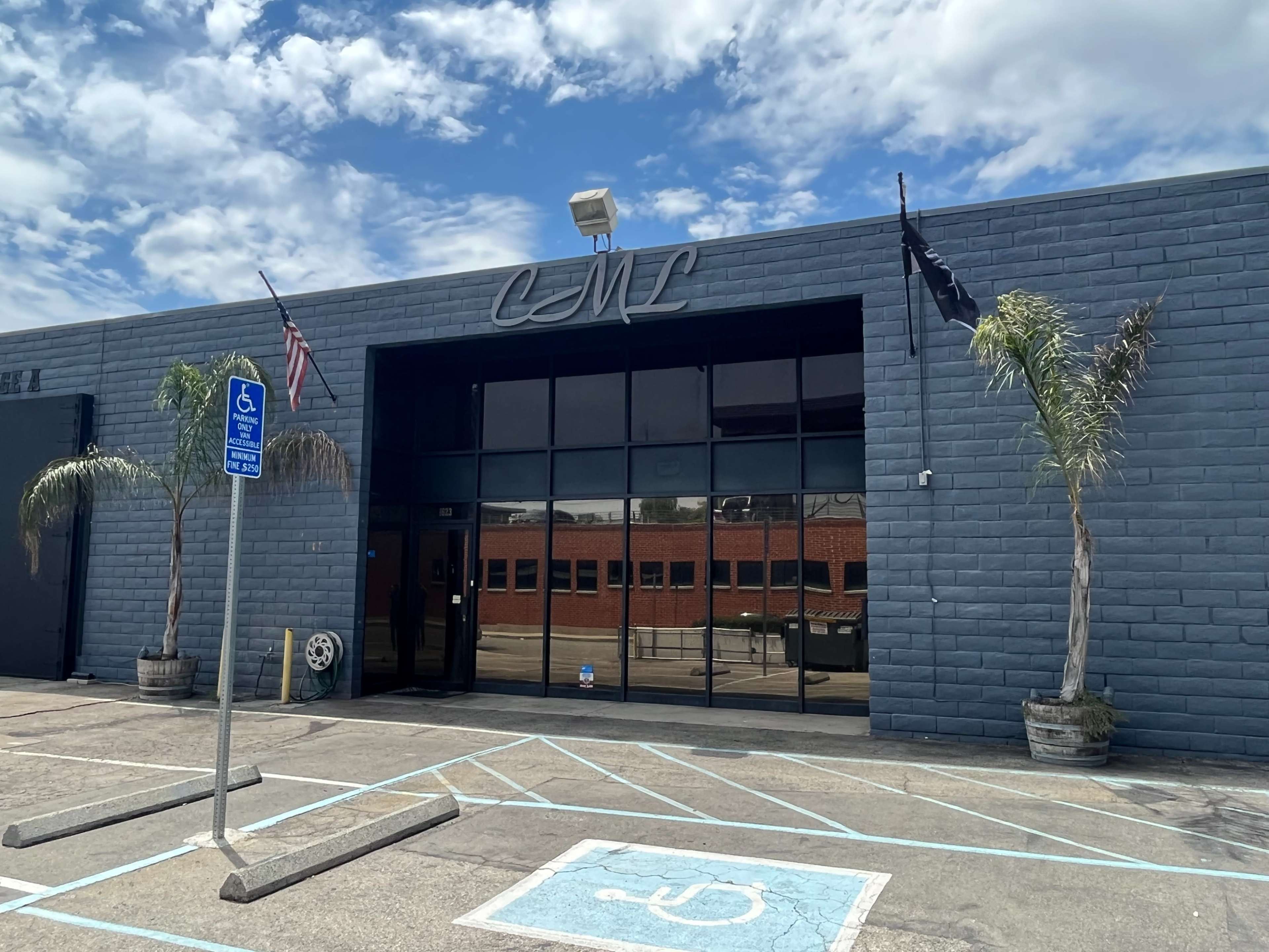 The image shows a modern commercial building with large glass windows, featuring the letters "CNT" above the entrance, and two palm trees flanking the front, along with a blue parking space marked for accessibility.