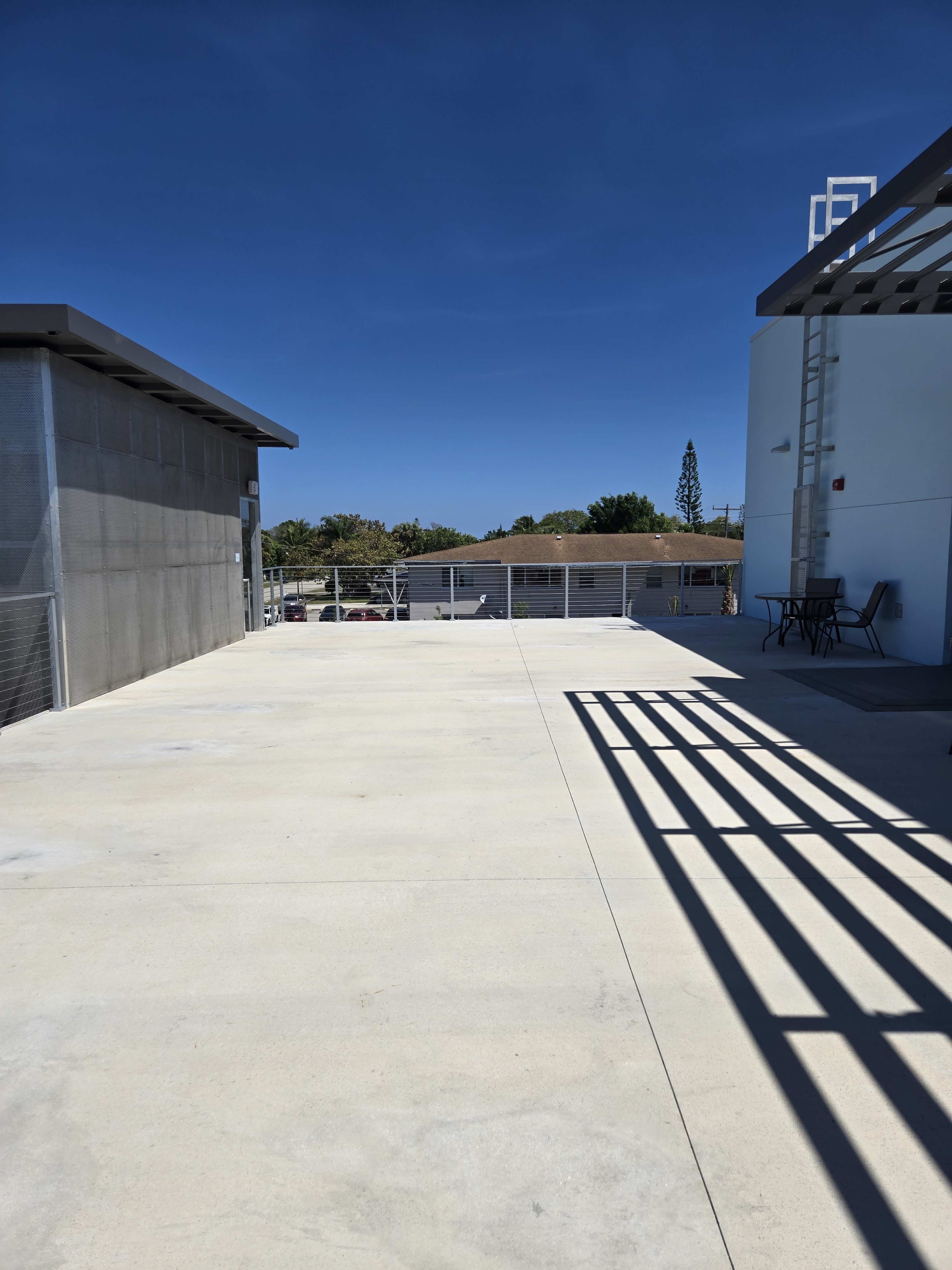 The image shows a spacious, sunlit rooftop area with concrete flooring and a few scattered structures in the background.