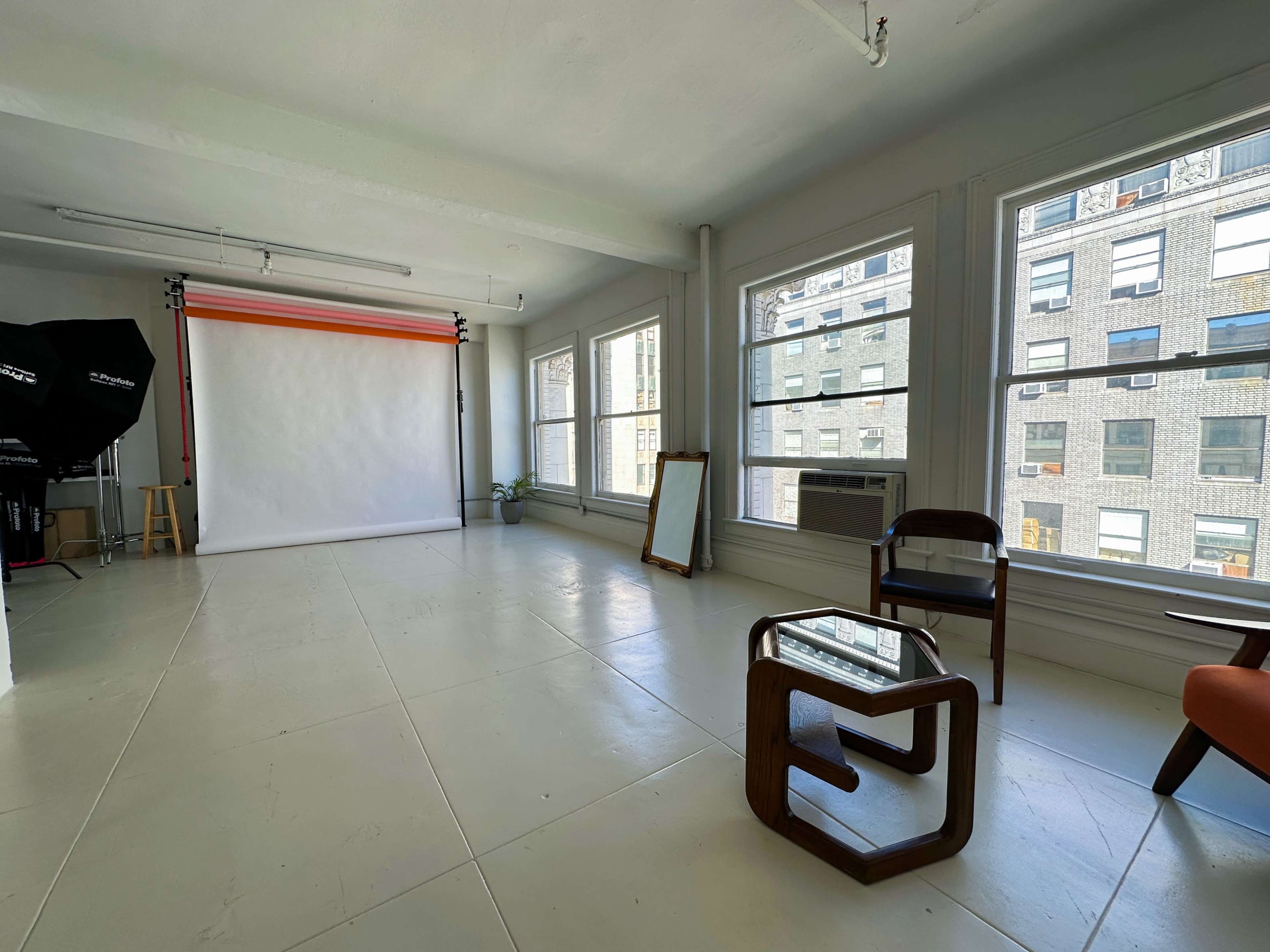 A spacious, brightly lit studio with large windows, a backdrop setup, and minimalist furniture.