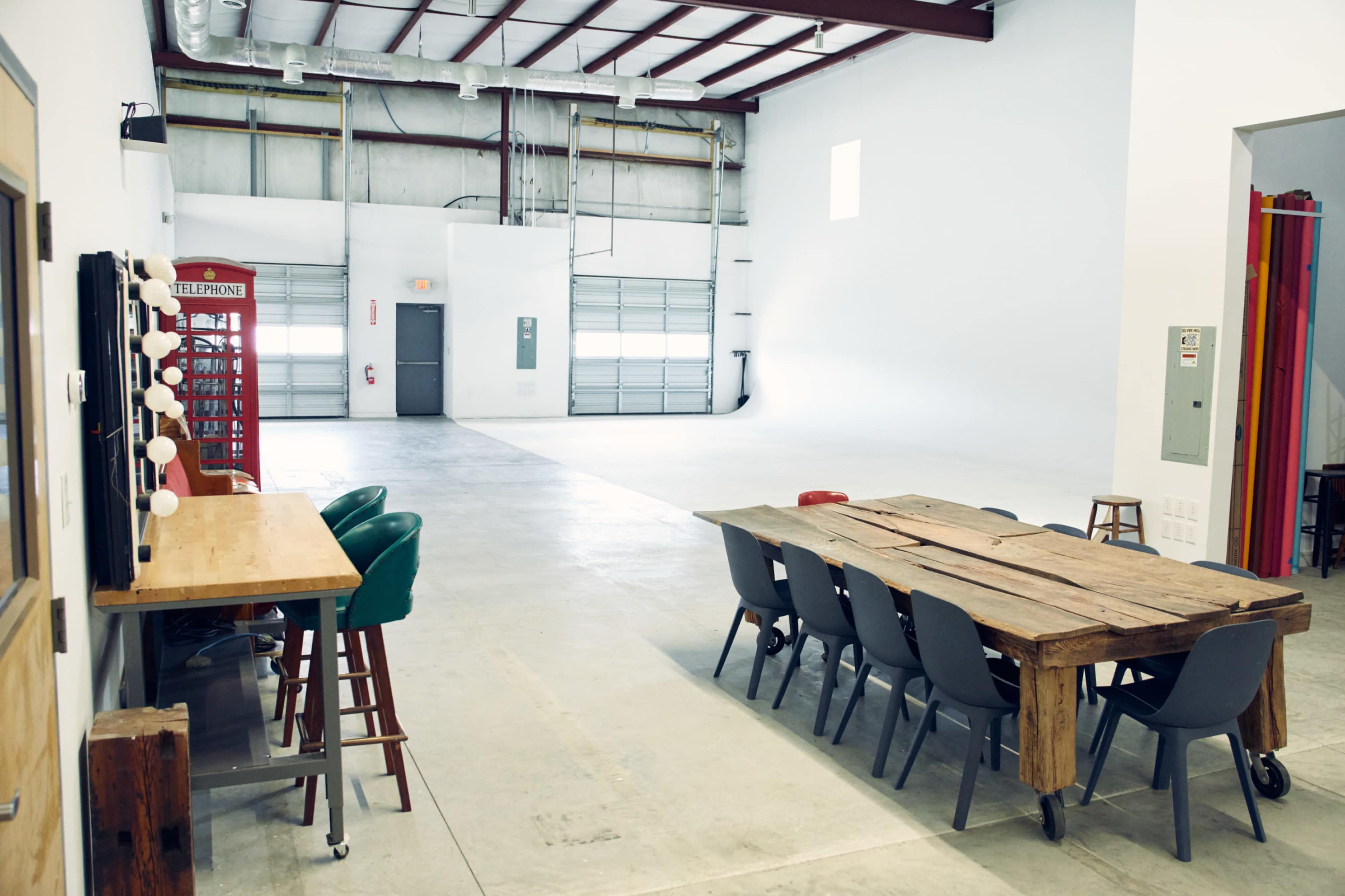 The image shows a spacious, industrial-style room with a long wooden table, chairs, and a vintage telephone booth in the background.