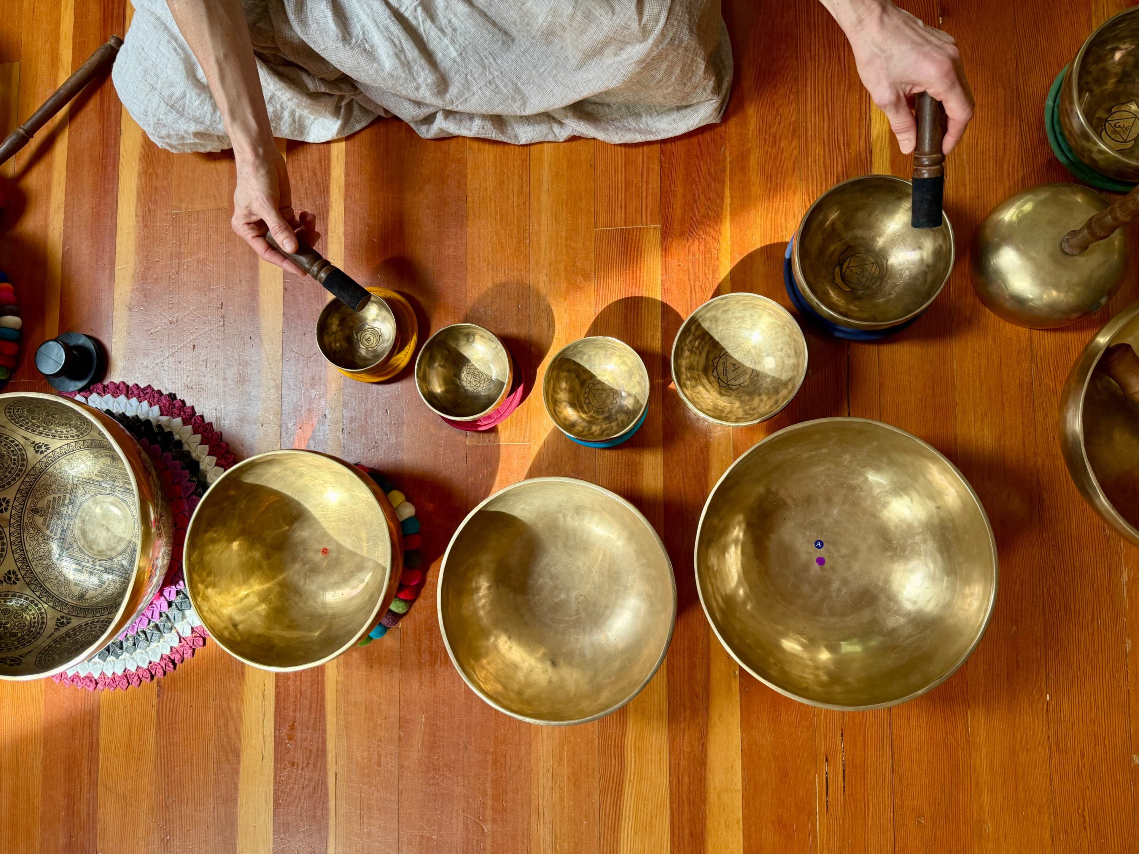 A person is arranging a series of Tibetan singing bowls of various sizes on a wooden floor.