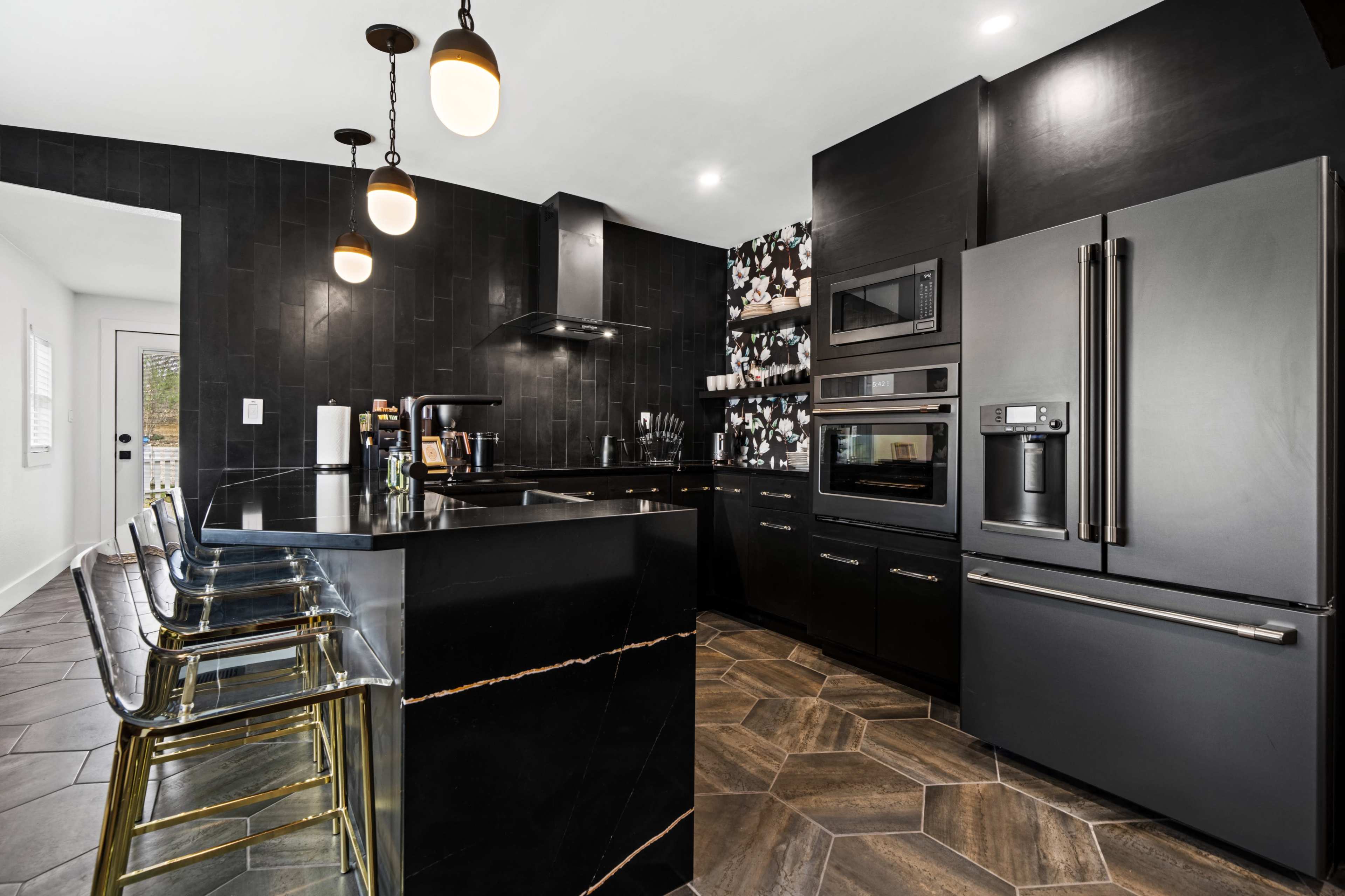 The kitchen features black cabinets and appliances, a contrasting floral accent wall, and a geometric tile floor, with bar stools at the island.