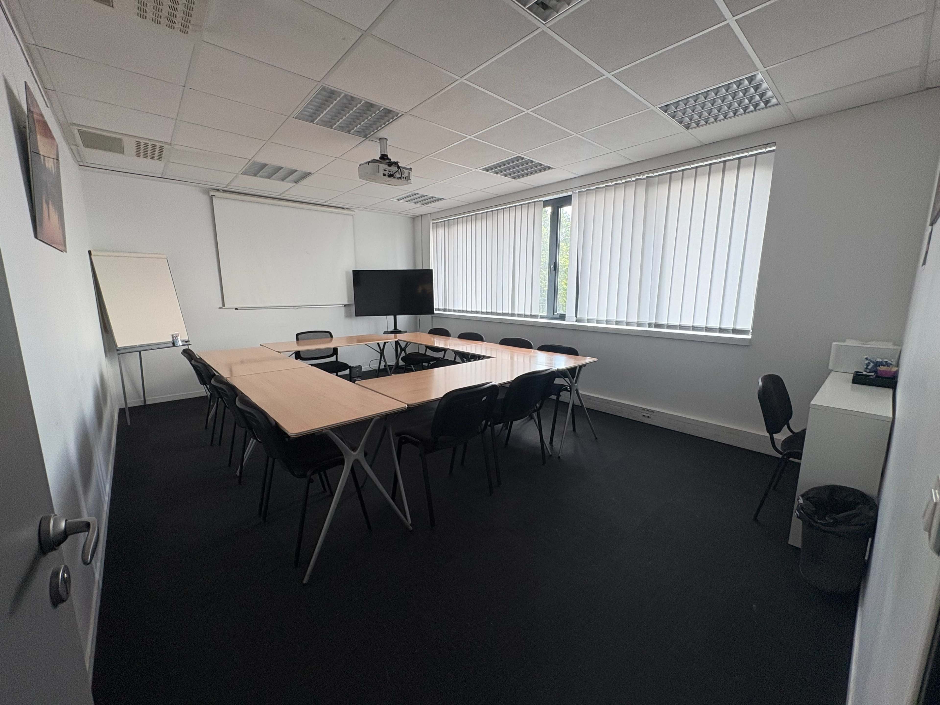 A meeting room with a large table surrounded by chairs, a projector, and a TV screen on the wall.