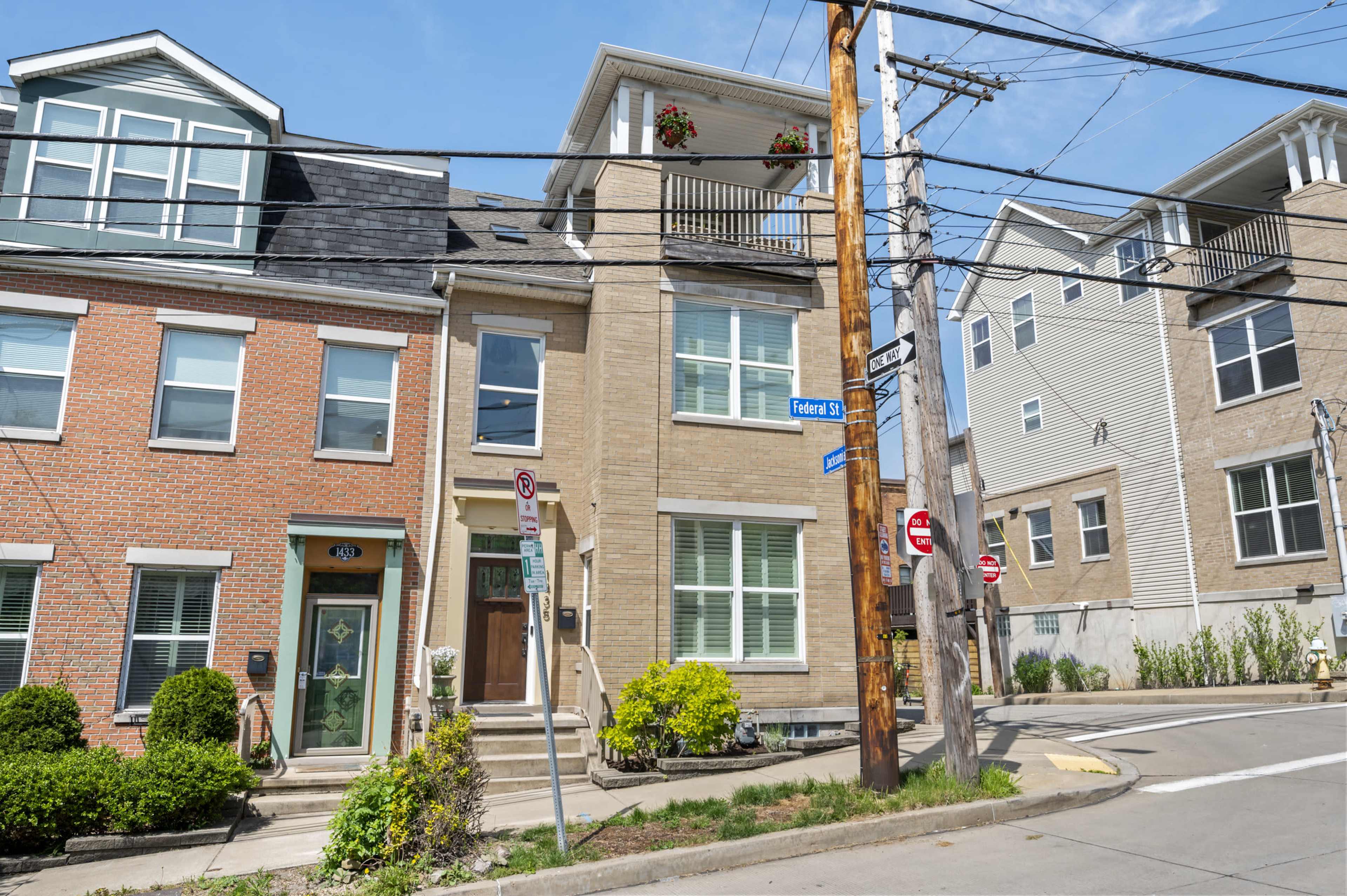 A multi-unit brick building on a corner lot, with a porch and several windows, surrounded by utility poles and adjacent structures.