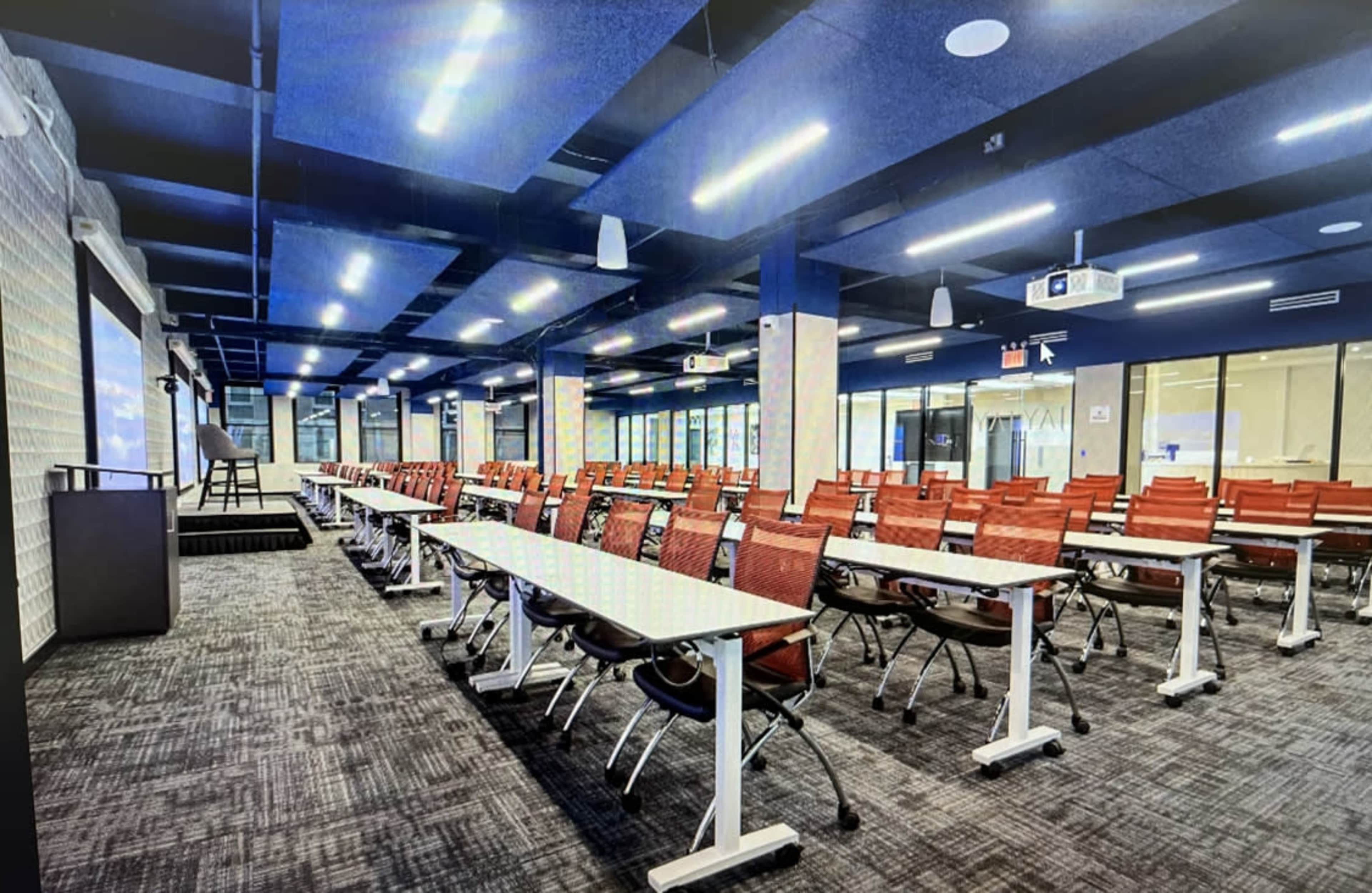 The image shows a large, modern conference room with multiple rows of empty red chairs arranged in front of white tables.