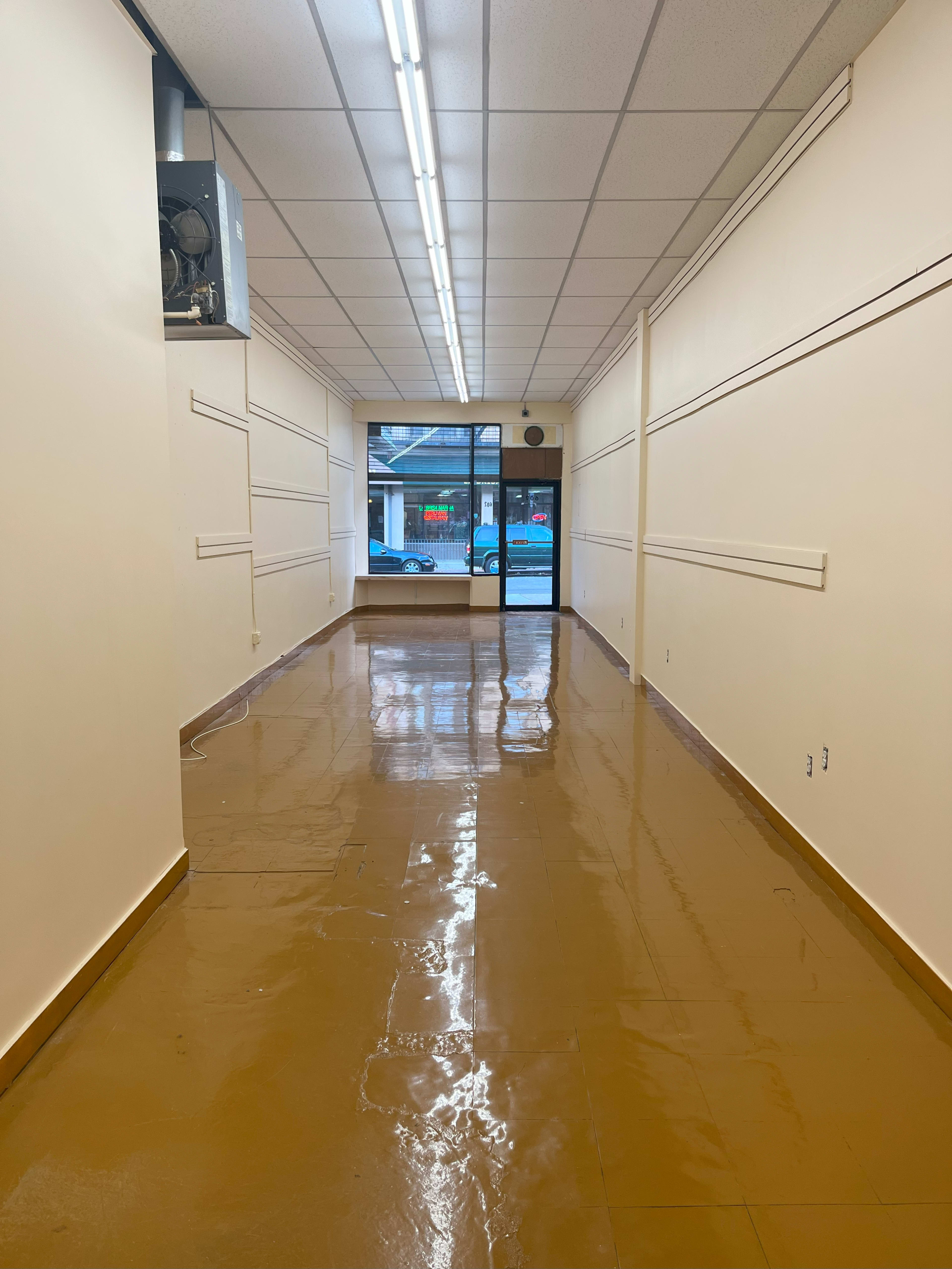 A long, empty hallway with a shiny brown floor and large windows at the far end.
