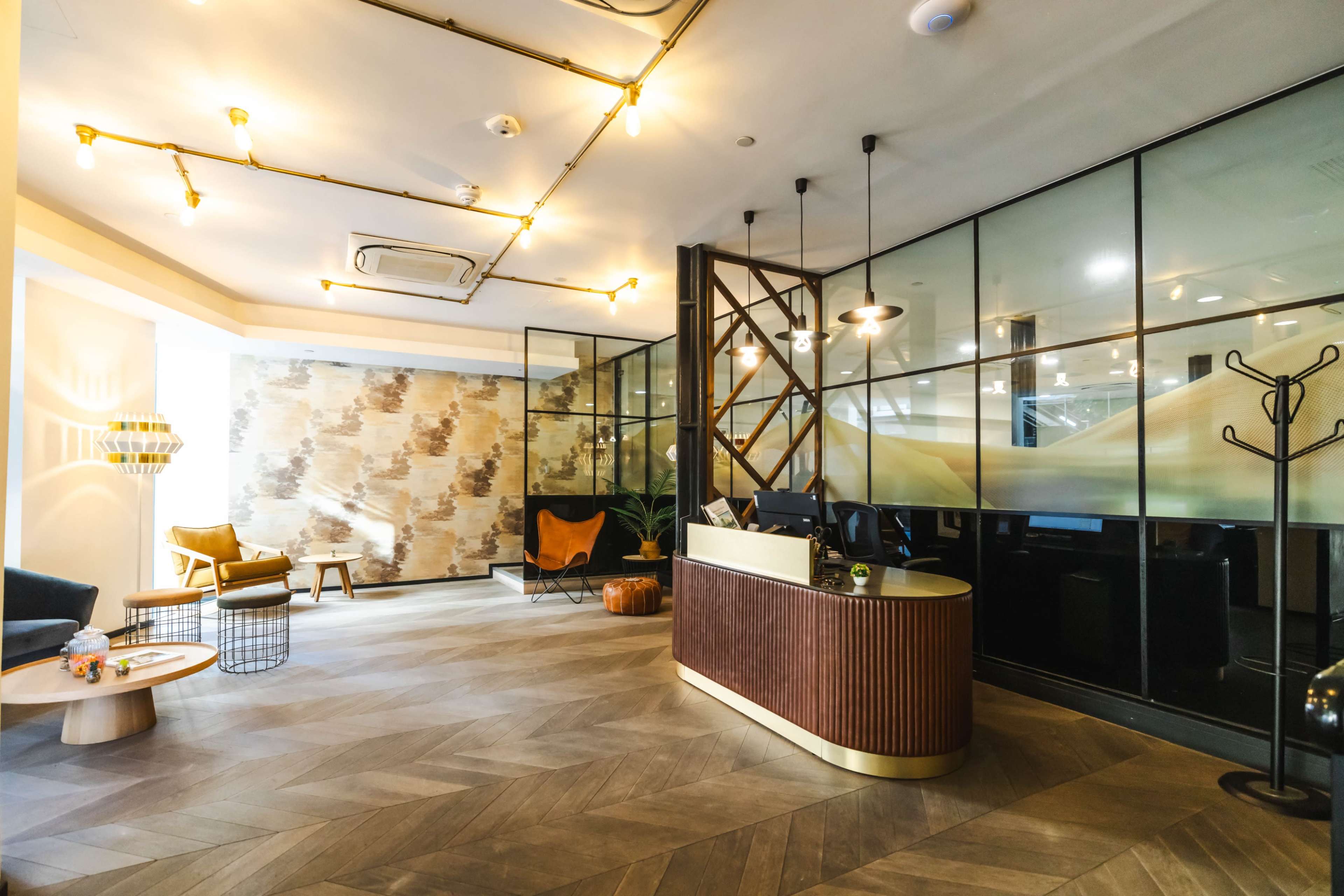 A modern reception area features a wooden desk, large glass panels, stylish lighting, and contemporary furniture arrangements.