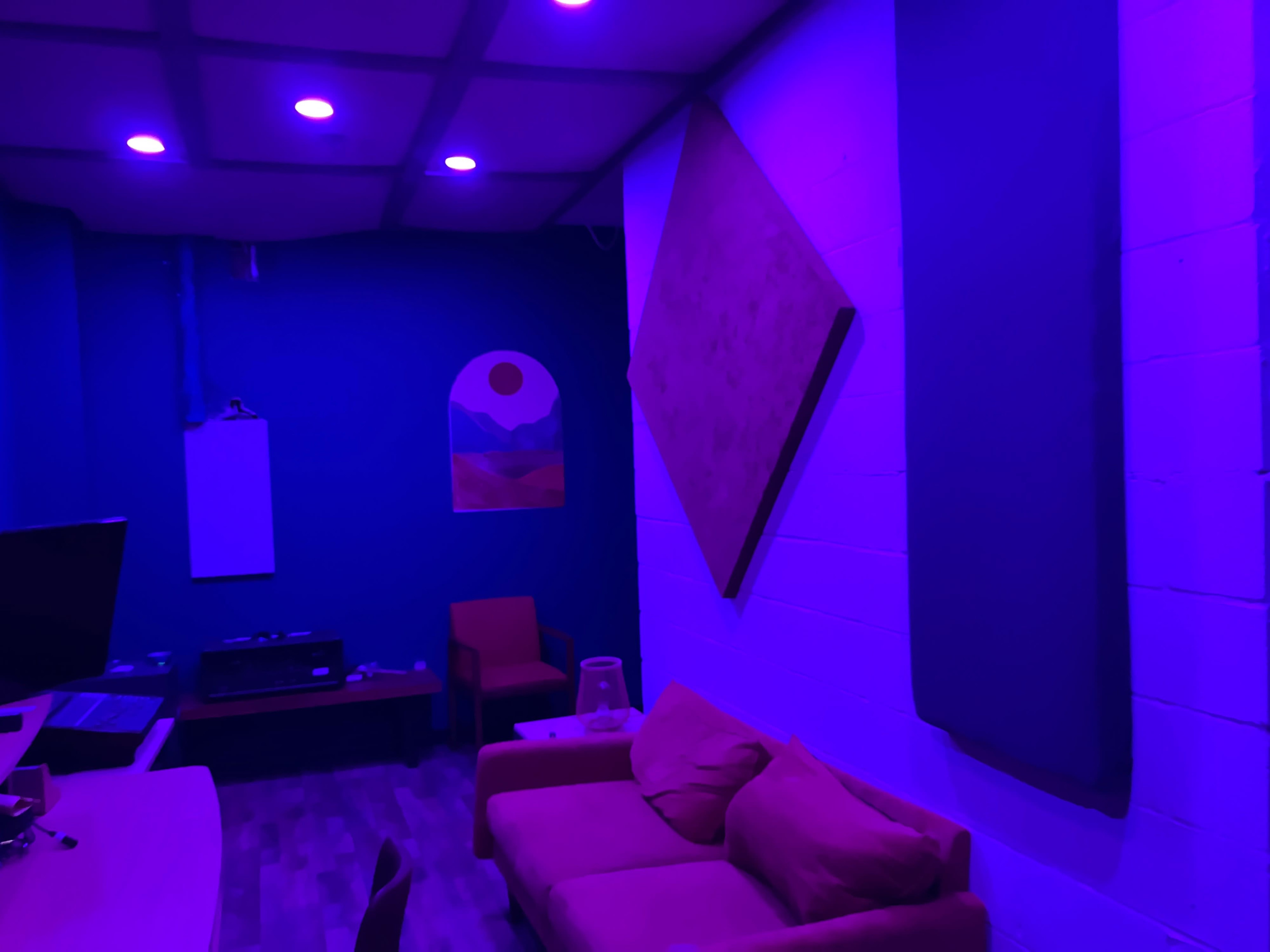 The image shows a room with blue walls, purple lighting, a sofa, a small table, and sound-absorbing panels on the walls.