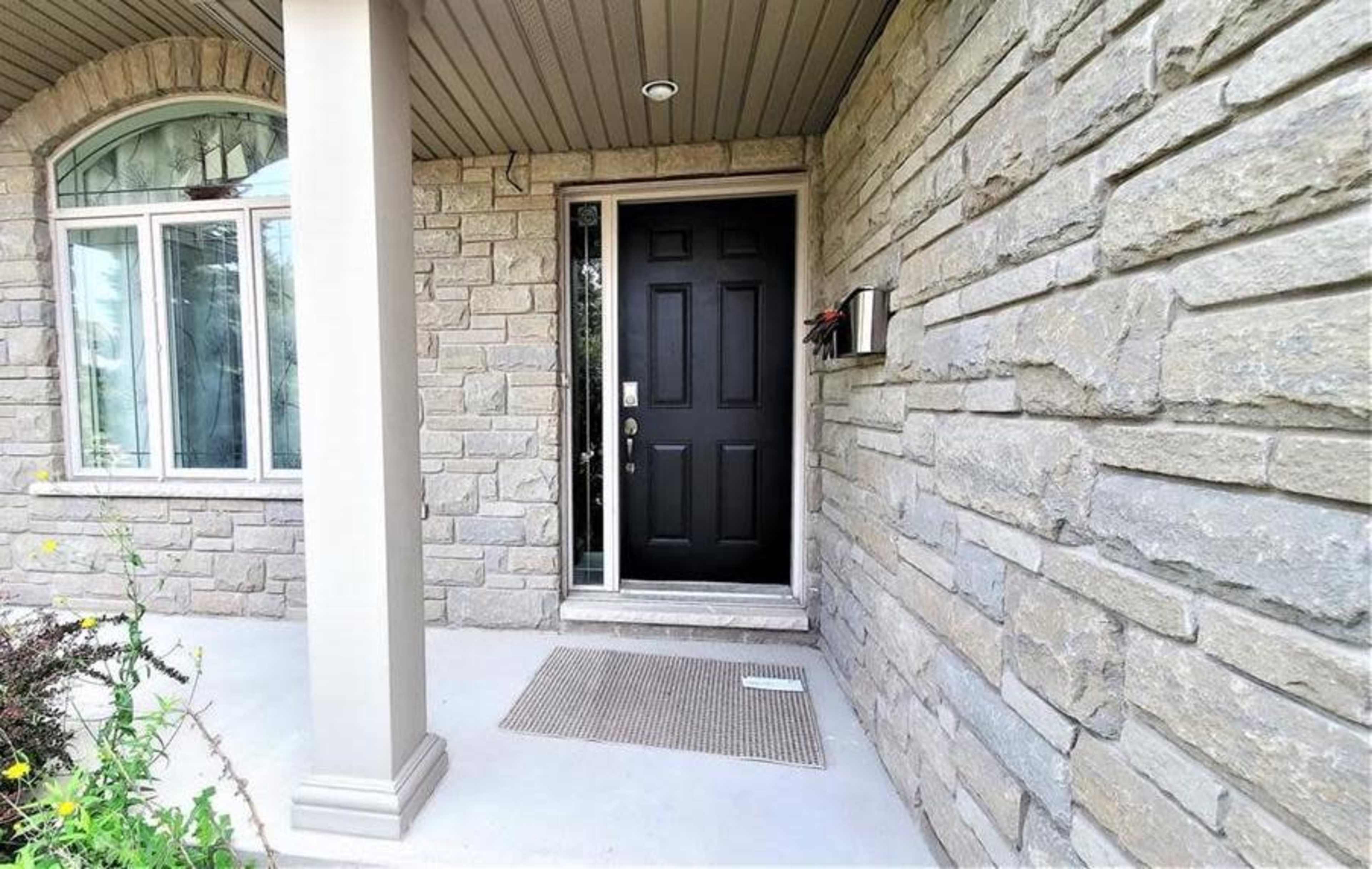 A front porch with a stone wall and a black door, featuring a welcome mat and a mail receptacle beside the entrance.