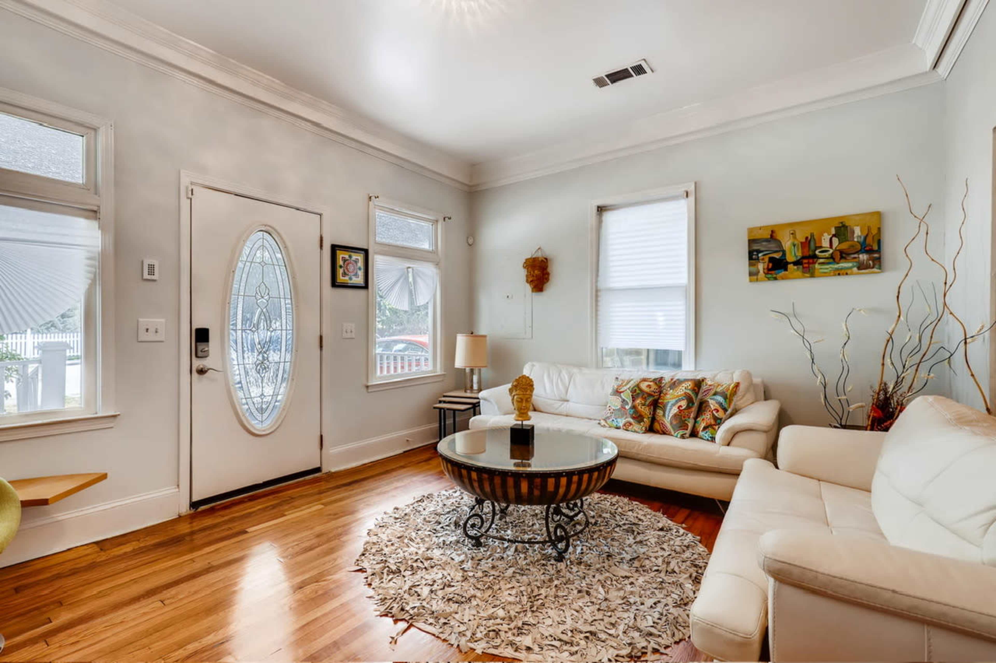The living room features a white sofa, a round coffee table on a decorative rug, and a door with a circular window leading outside.