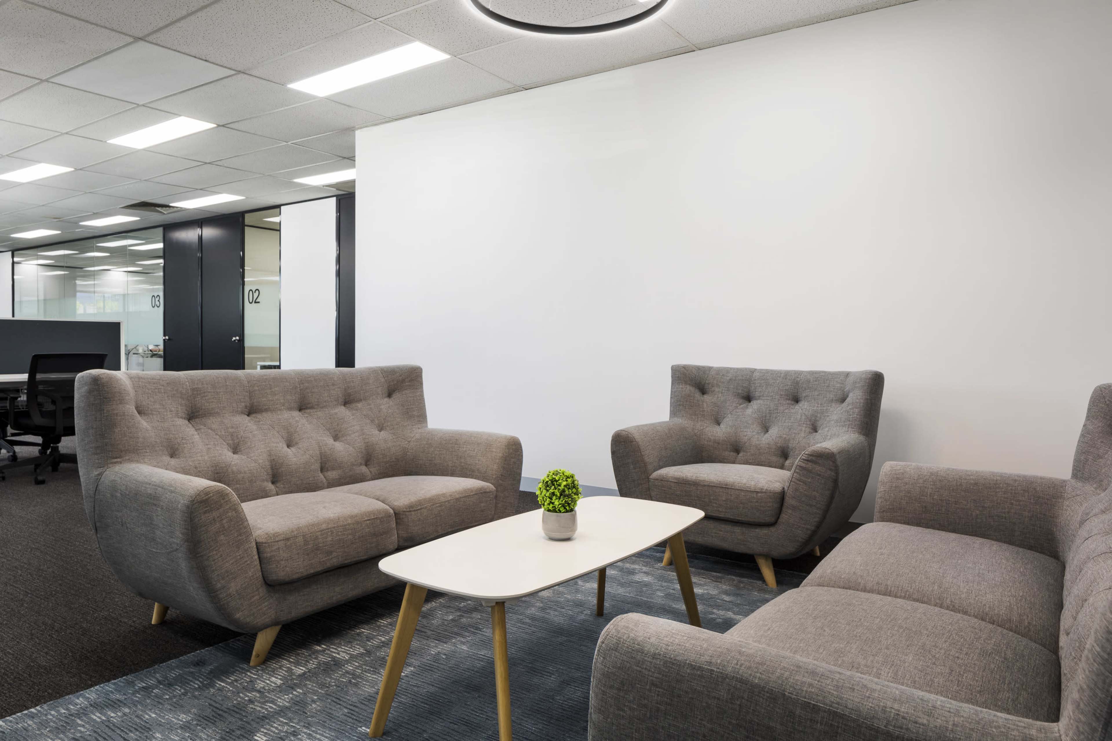 A modern office seating area features a gray upholstered couch and two matching chairs arranged around a small white table with a potted plant.