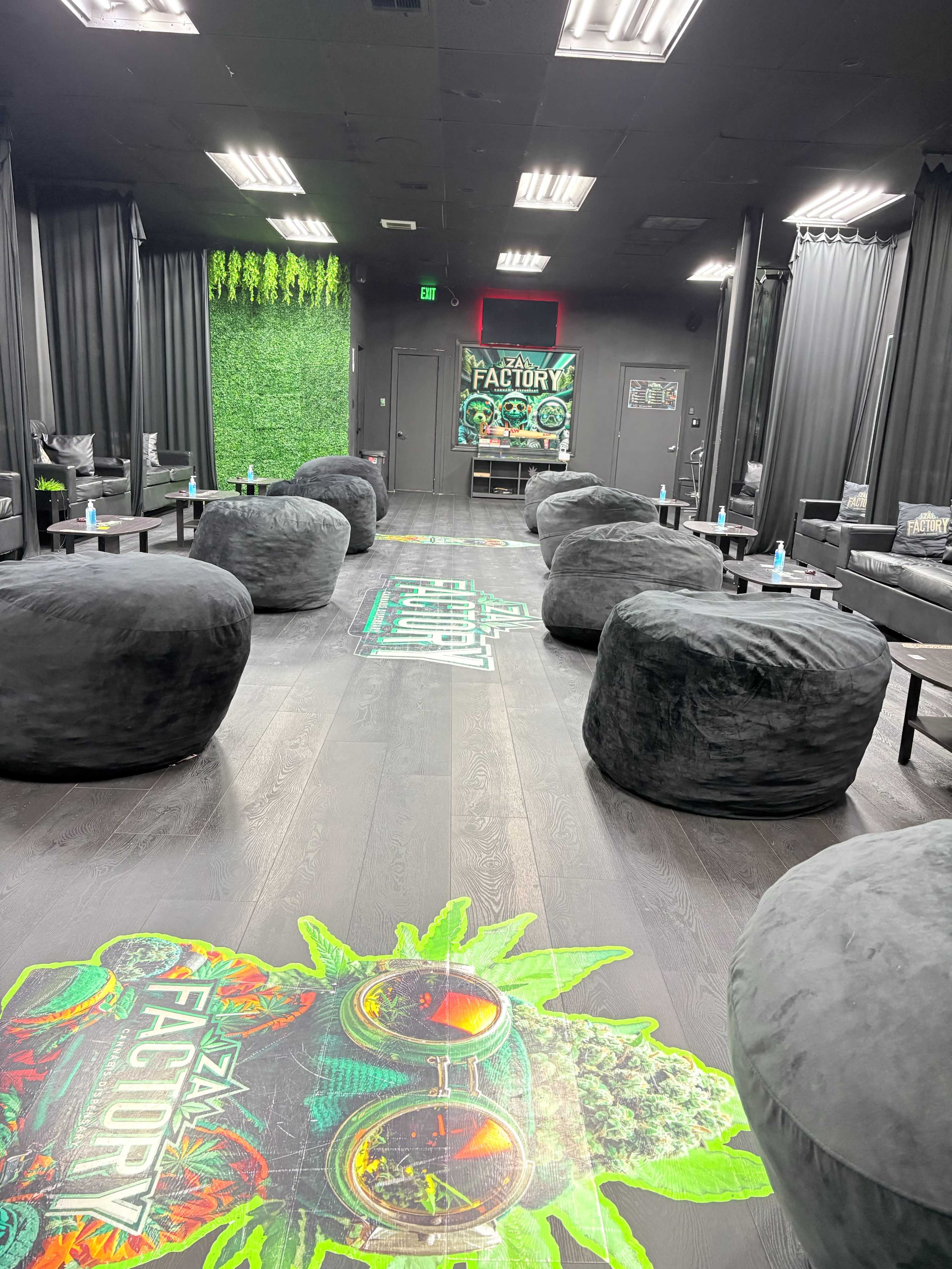 The image shows a lounge area with large, round bean bag chairs arranged on a floor featuring a colorful graphic design that includes the words "ZMJ FACTORY" surrounded by plants.