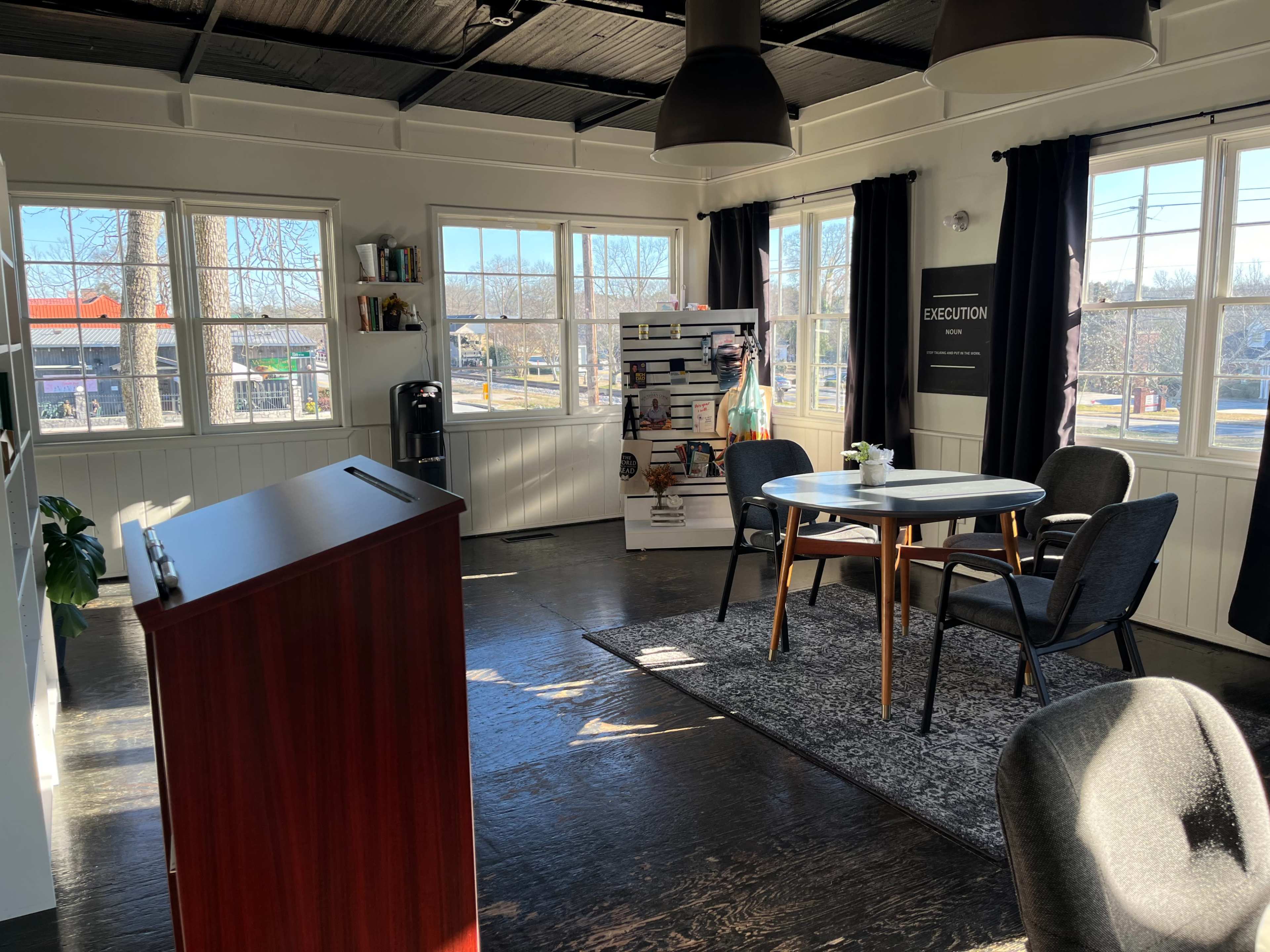 A bright, modern office space with a round table and chairs, a podium, and large windows allowing natural light to enter.
