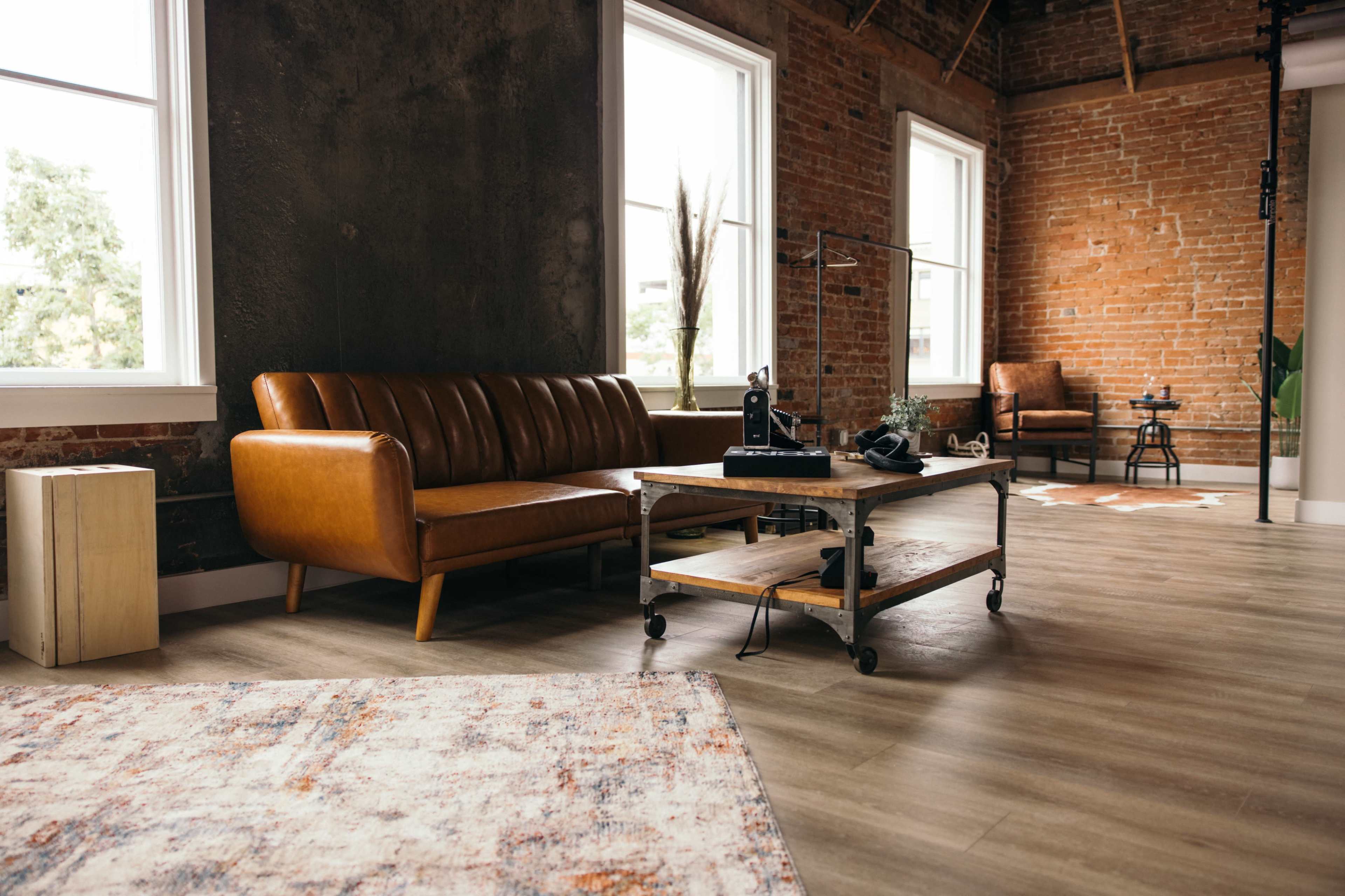 A modern interior space featuring a brown leather sofa, a wooden coffee table on wheels, and large windows that let in natural light.