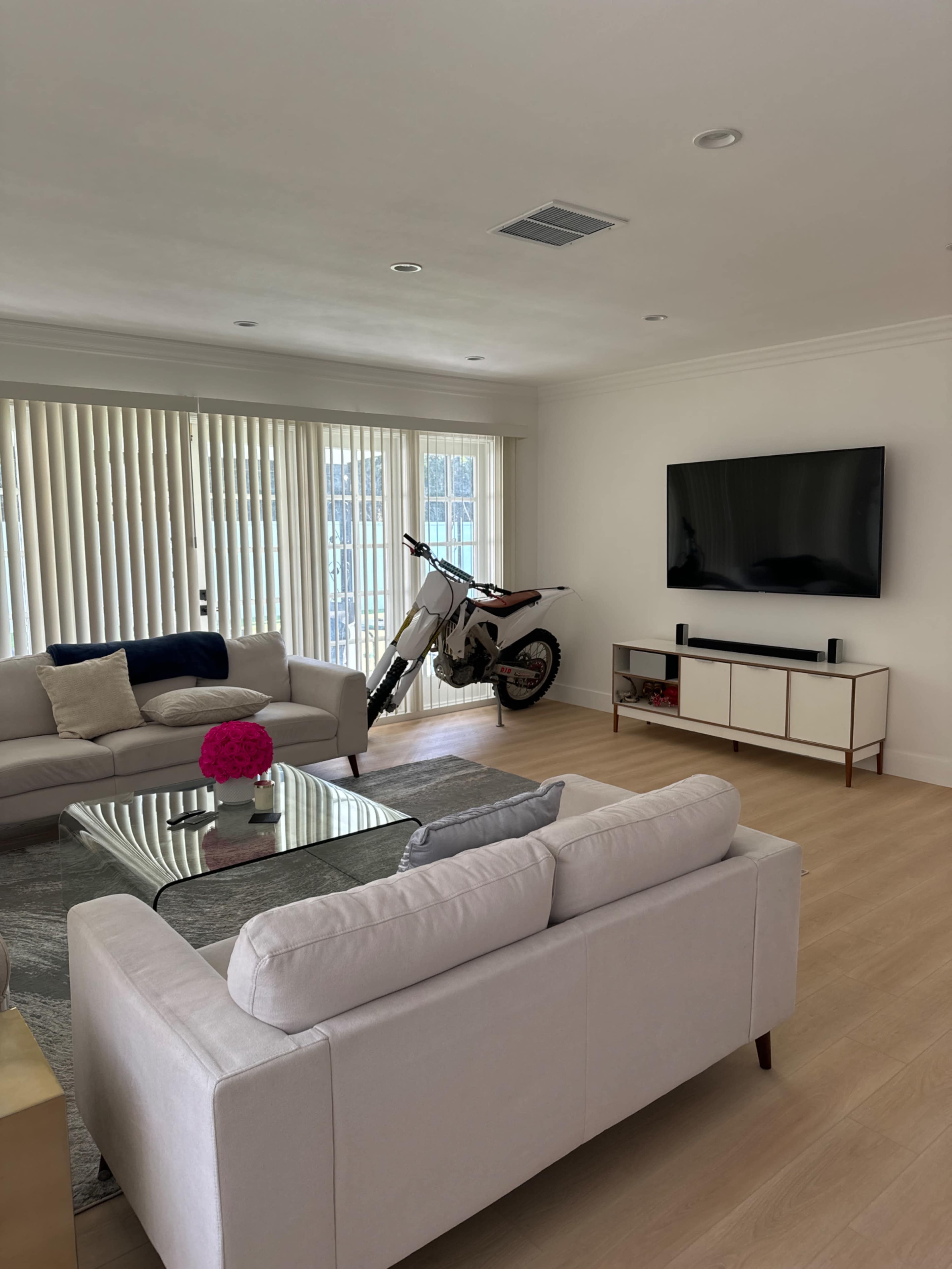 A modern living room features a dirt bike beside a couch and a television mounted on the wall.