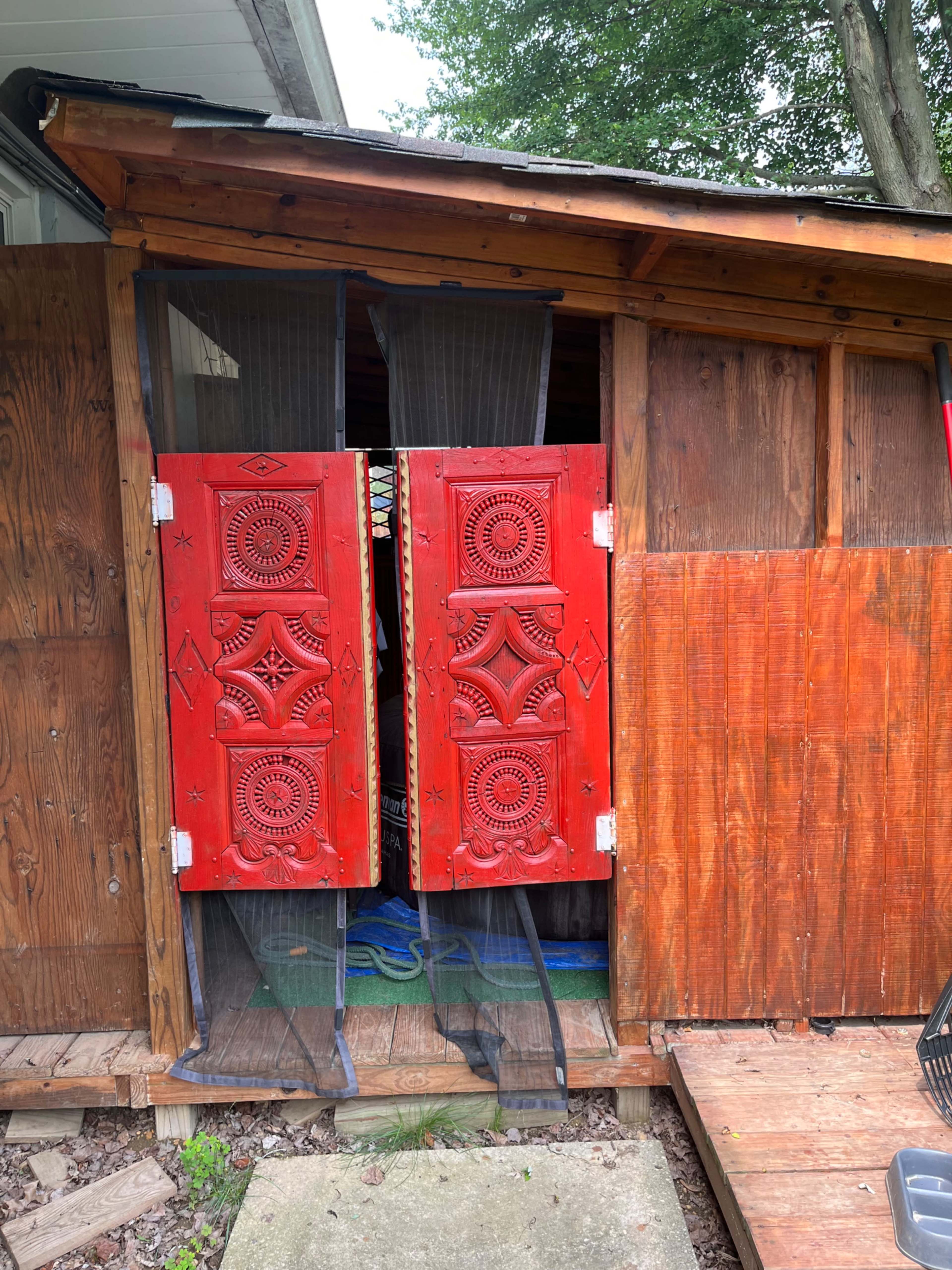 A wooden structure with red carved double doors partially open, revealing a mesh curtain behind them.