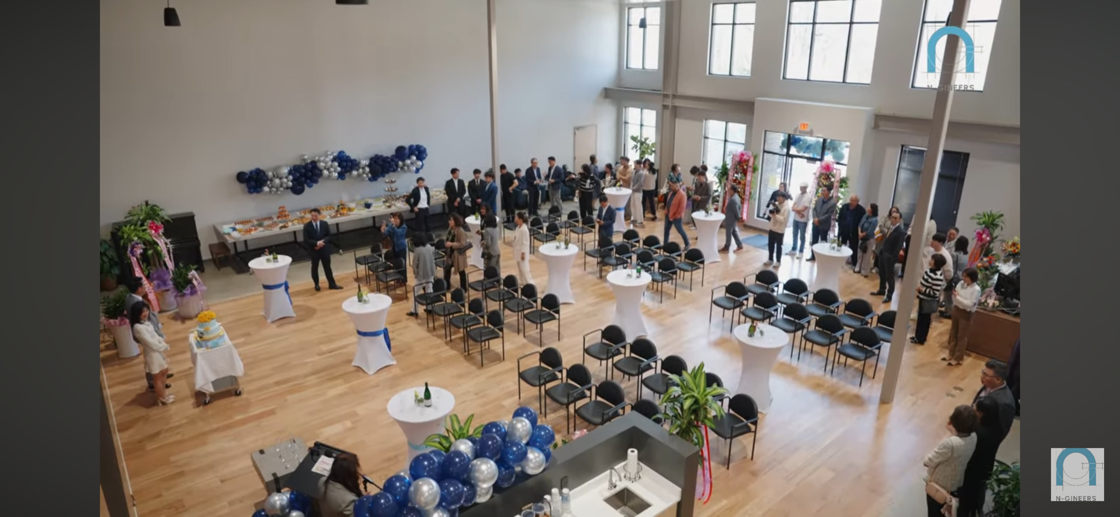 An event is taking place in a spacious hall with guests mingling around tables and snacks displayed along one wall.