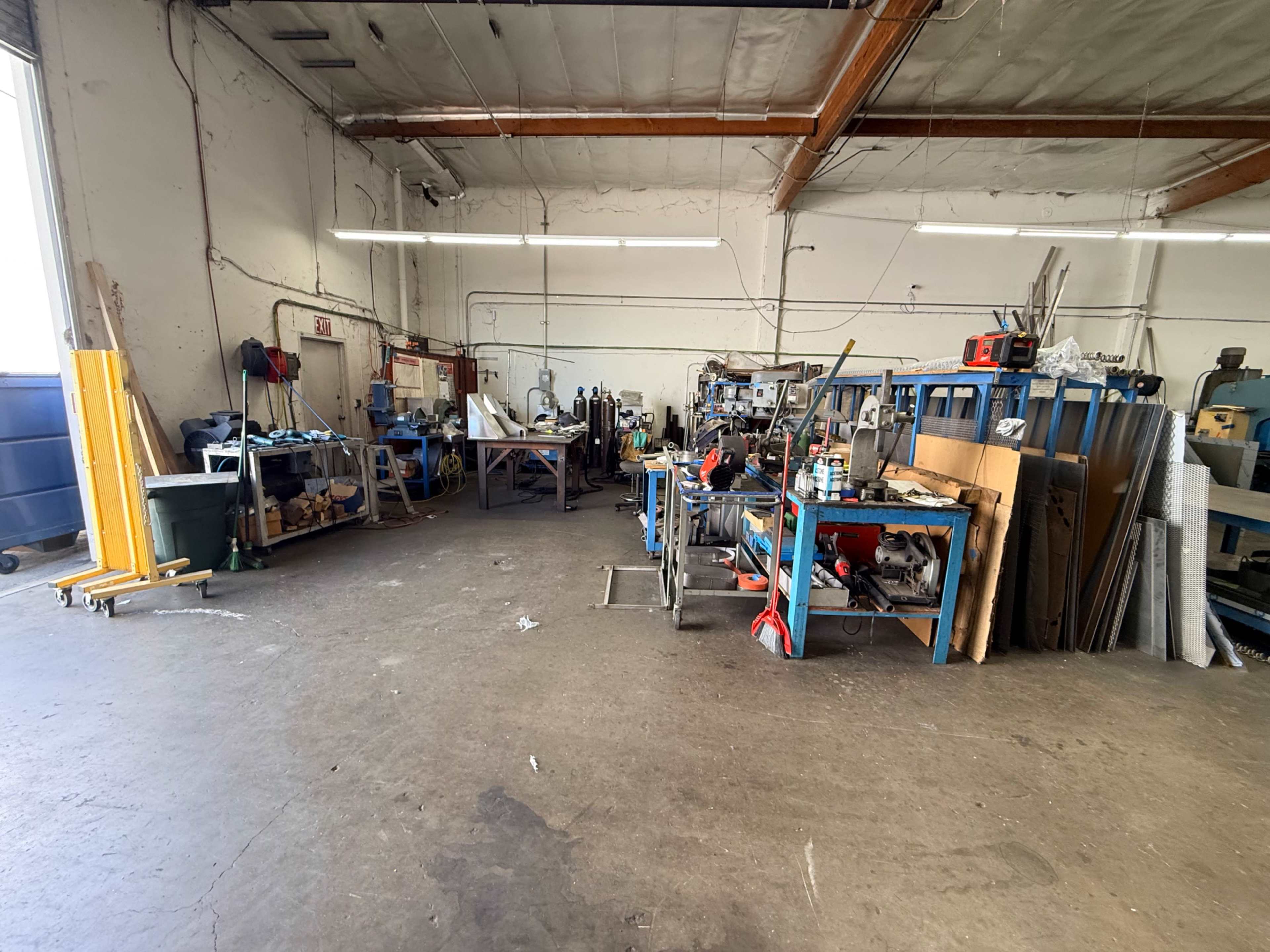 The image shows a workshop with various workstations, tools, and materials scattered throughout a spacious industrial area.