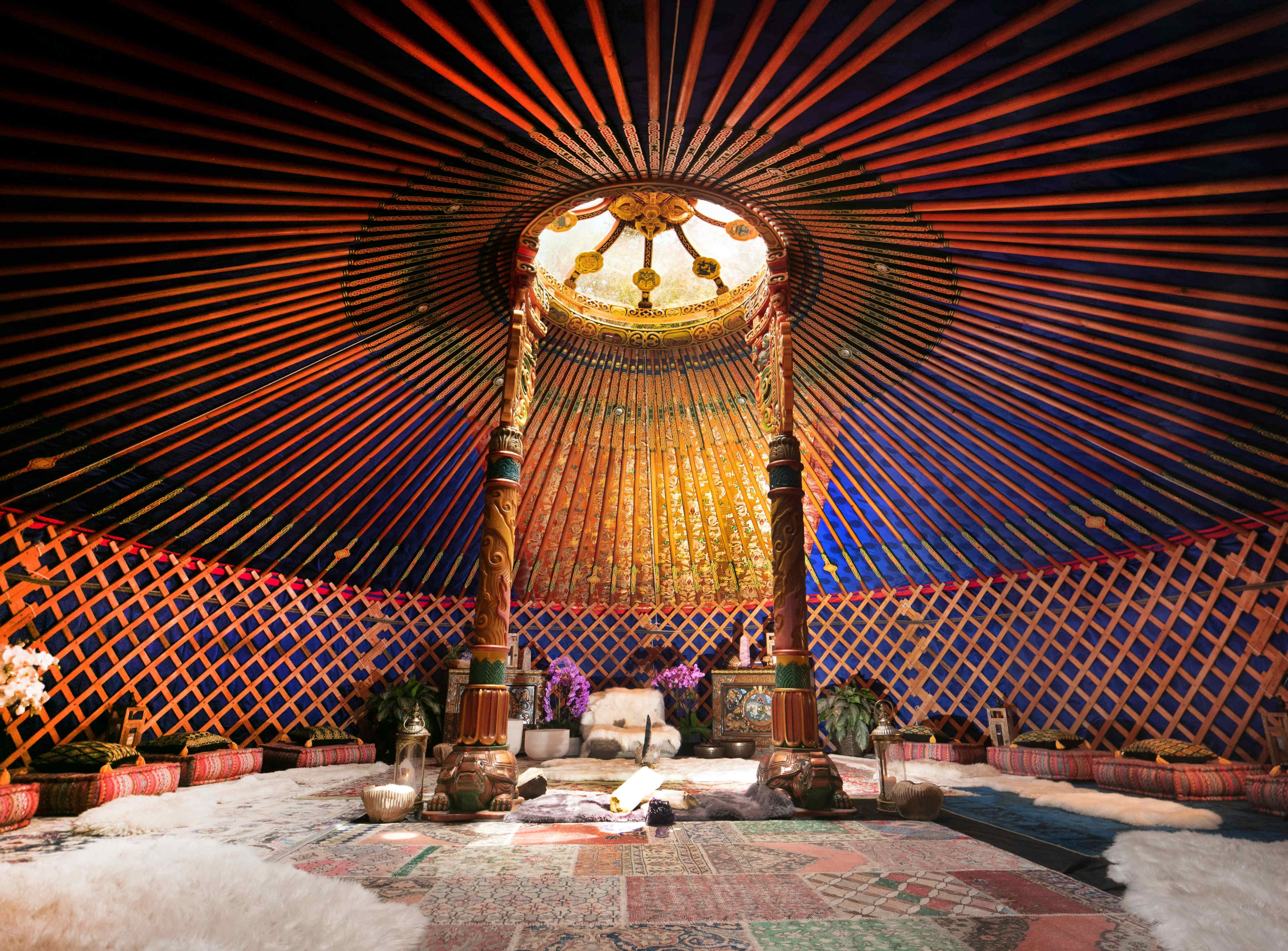 The interior of a yurt features a circular skylight, wooden pillars, and decorative walls adorned with vibrant patterns.