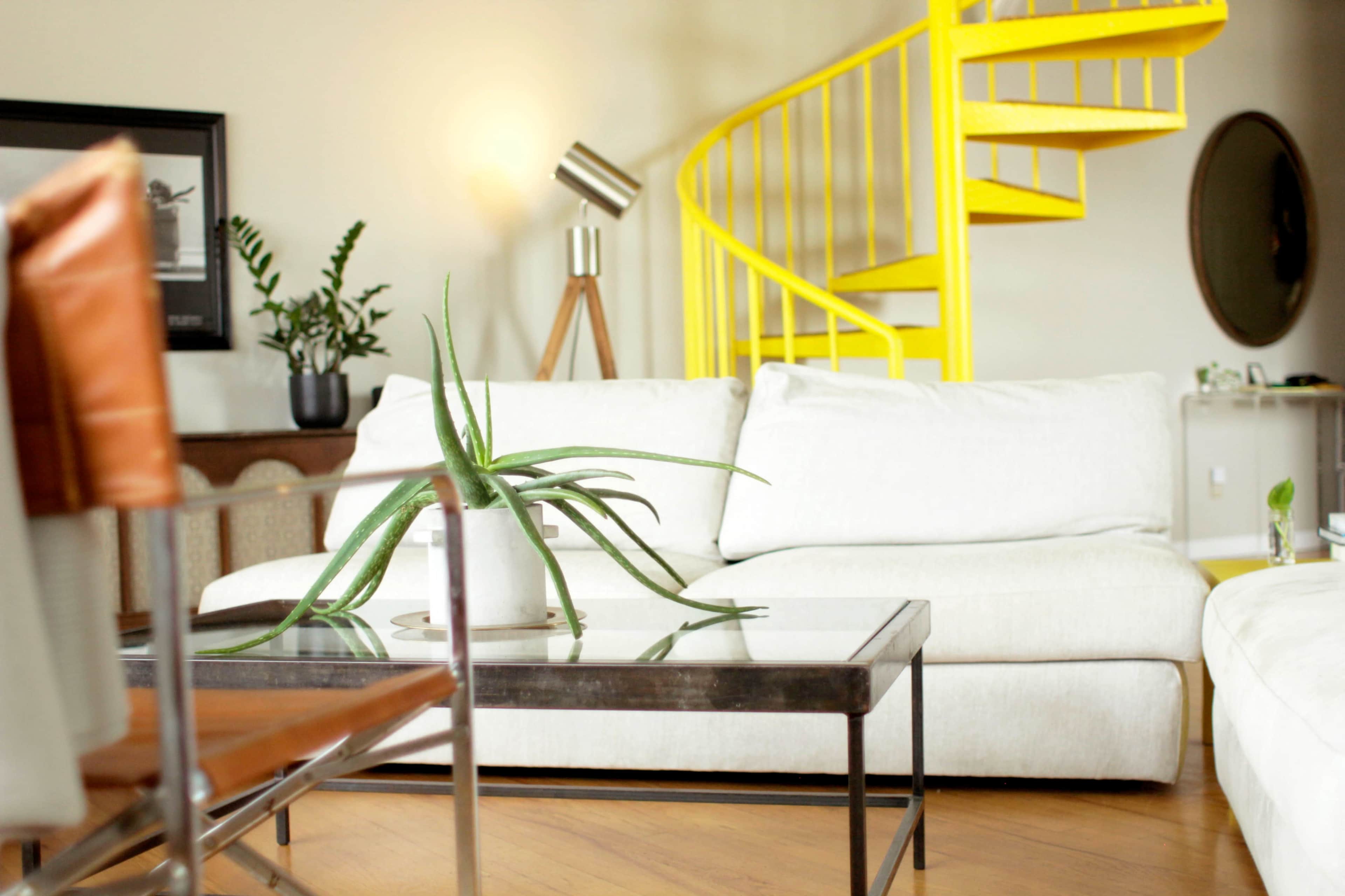 A modern living room features a white couch and a coffee table with a plant, alongside a spiral yellow staircase in the background.