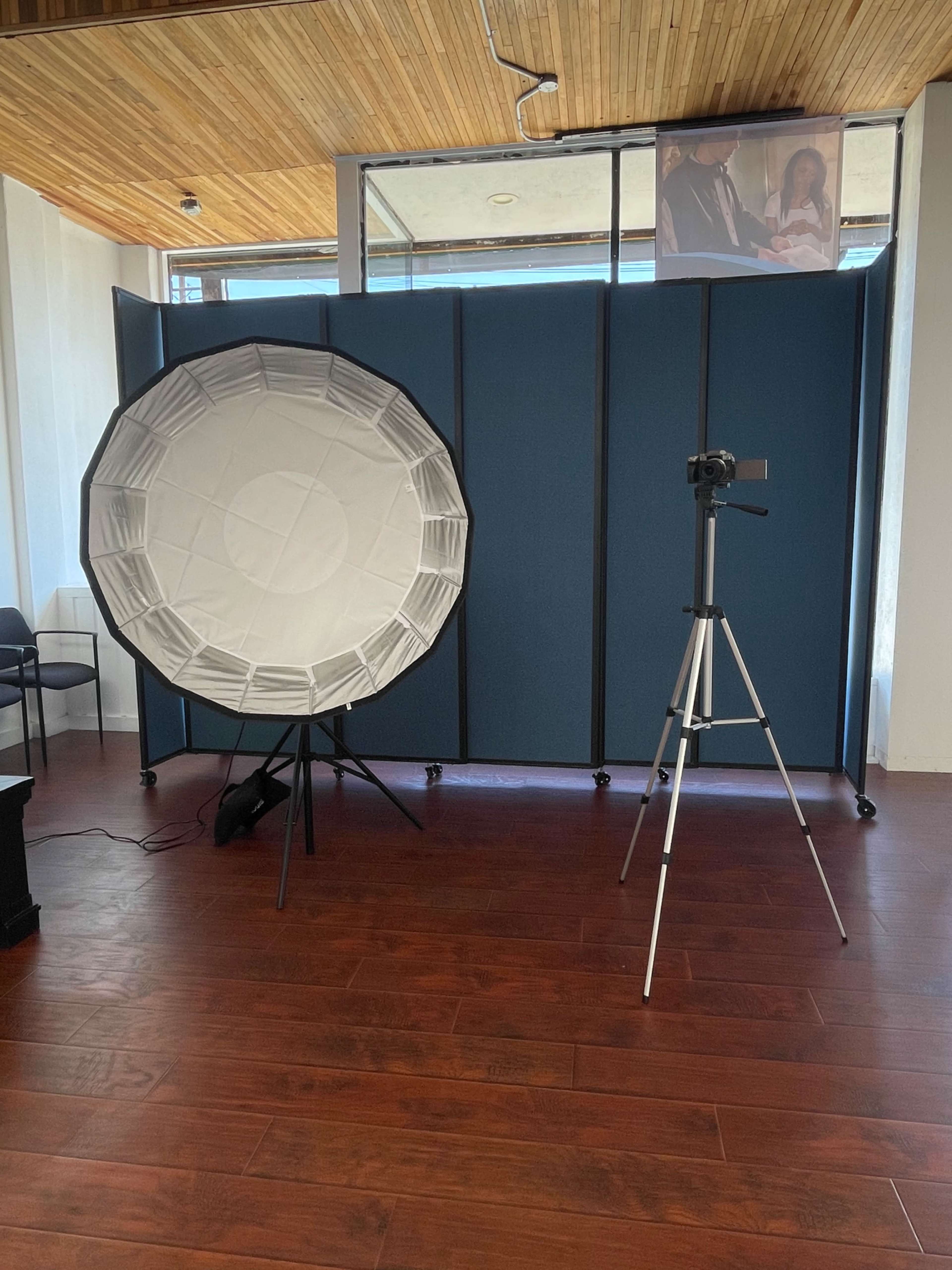 A photography setup with a large softbox and a camera mounted on a tripod, positioned in front of a blue divider.