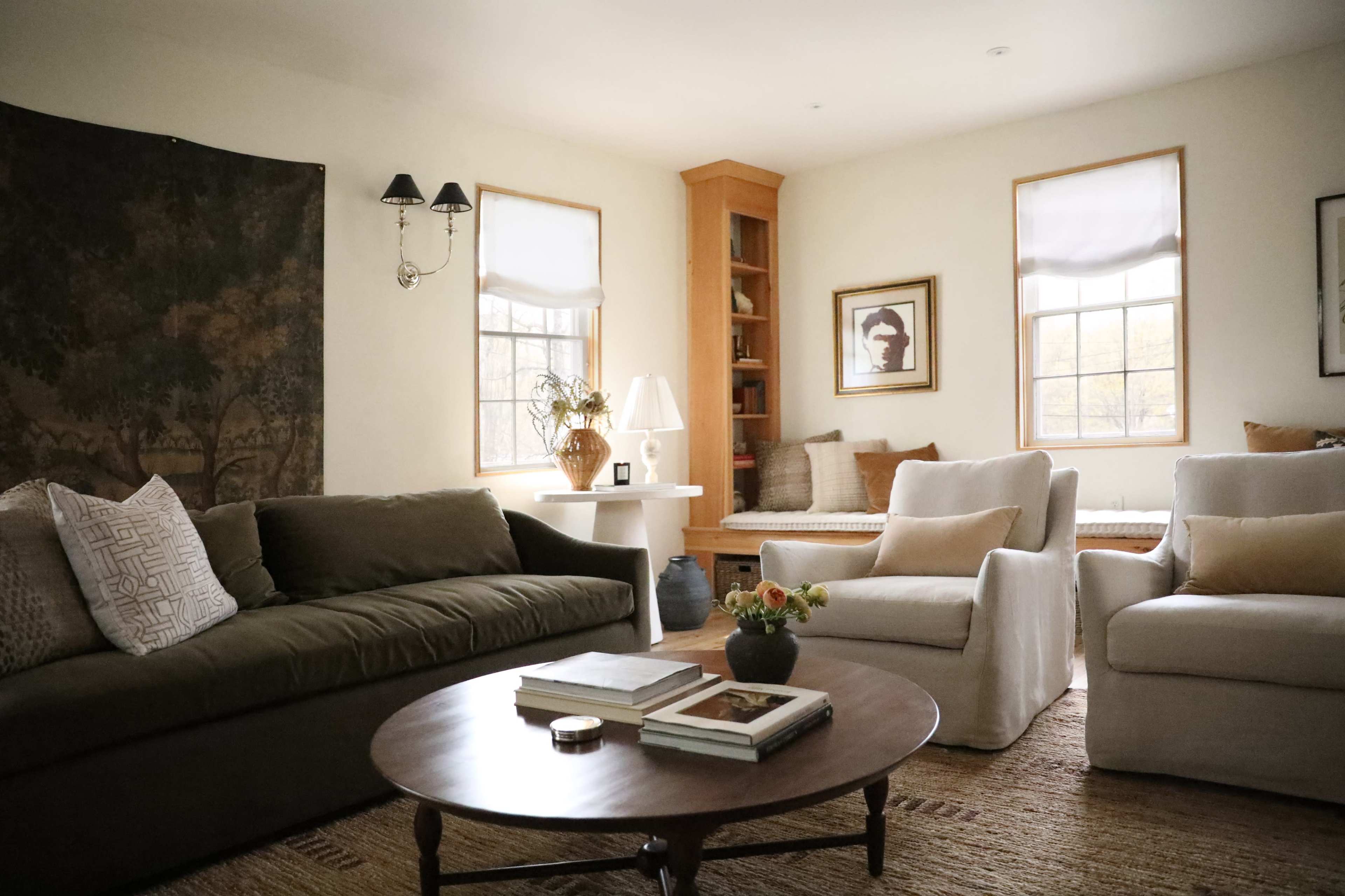 The living room features two sofas, a round coffee table, and built-in bookshelves, with natural light coming through the windows.