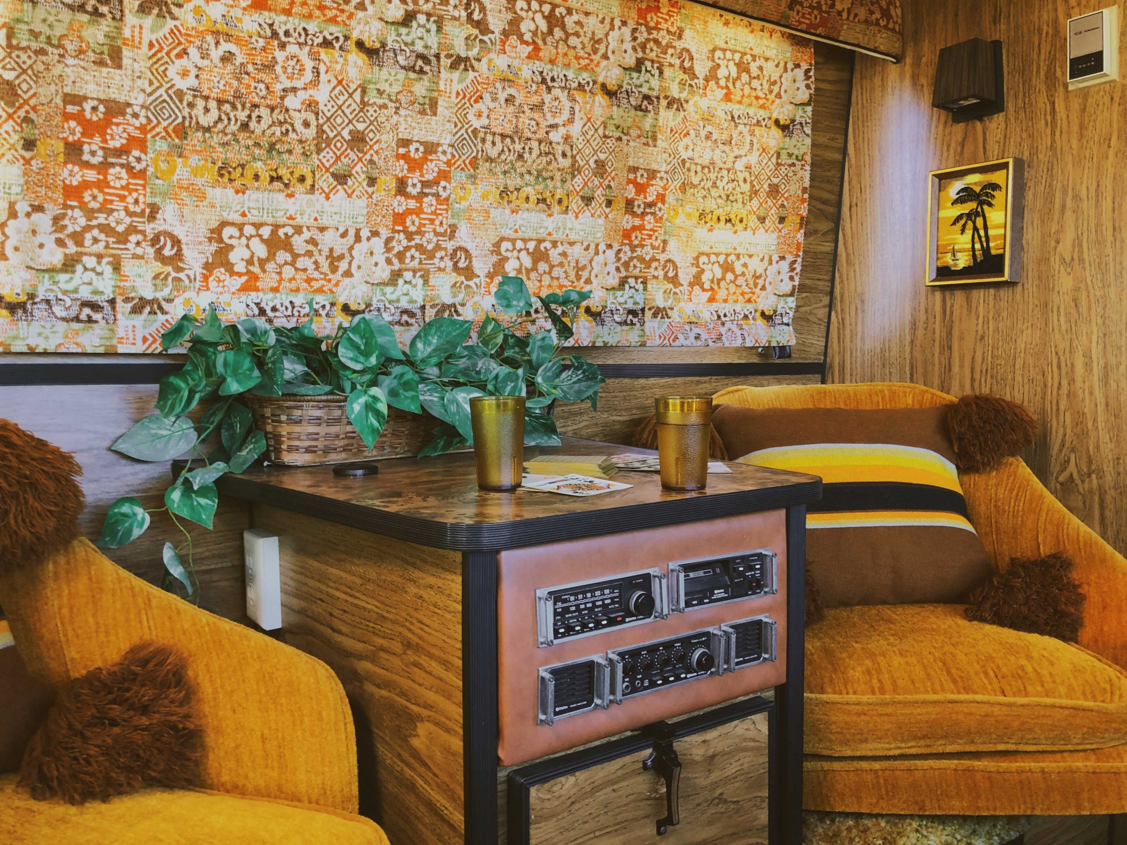 A cozy interior of a retro-themed room with orange armchairs, a wooden table, and patterned curtains.
