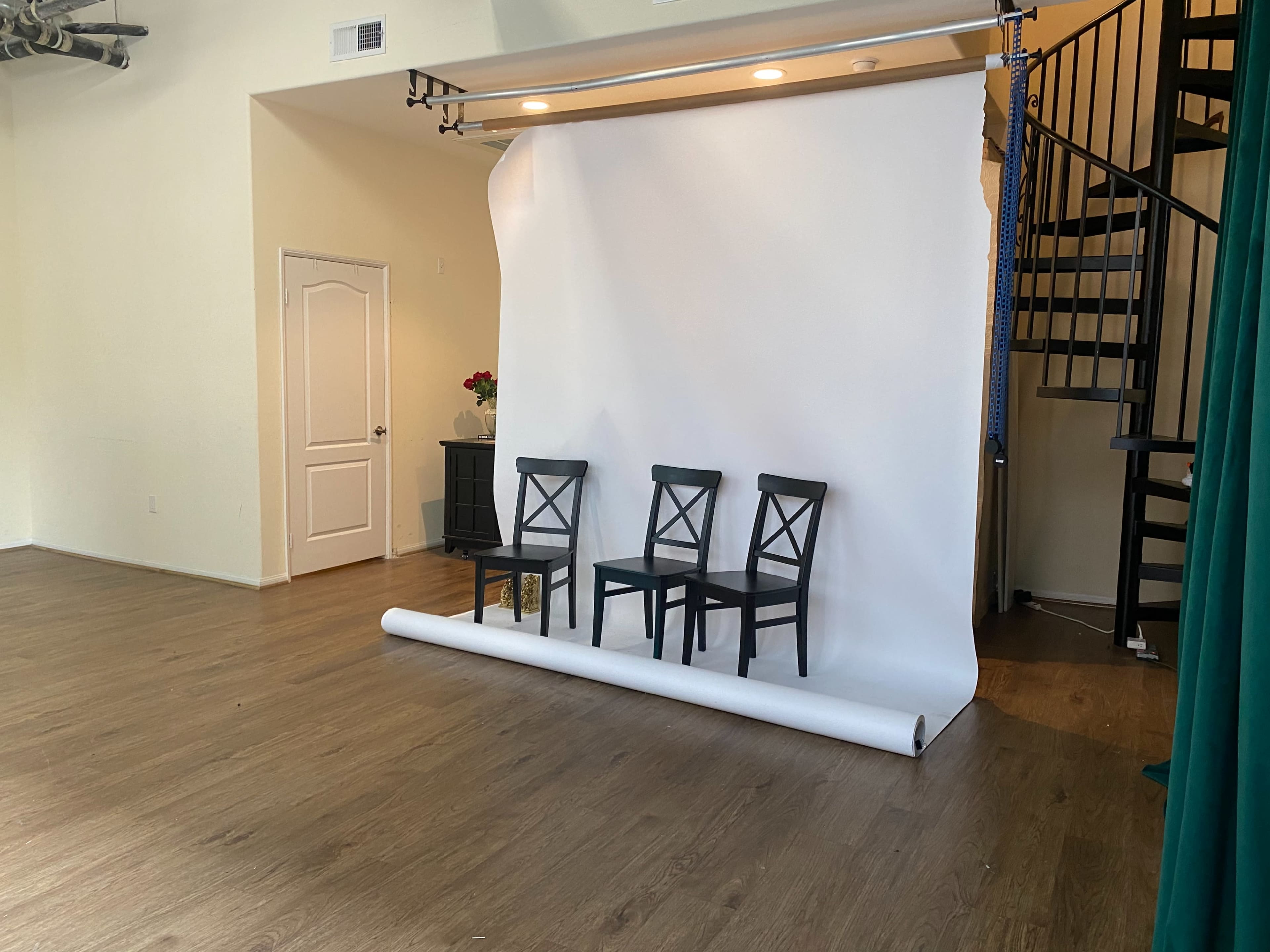 A spacious room with a white backdrop, three black chairs arranged in front, and a staircase in the background.