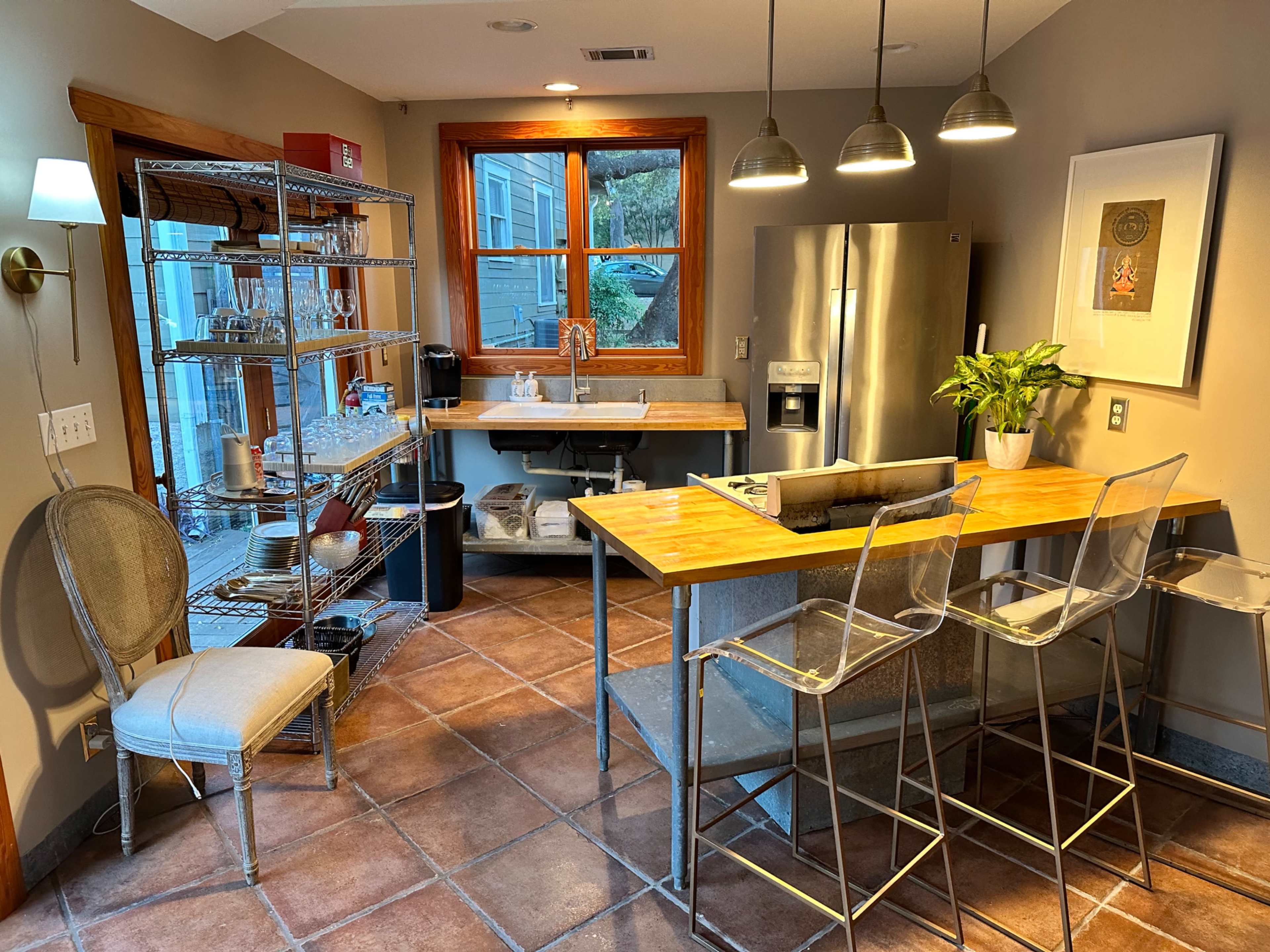 The image shows a modern kitchen with a countertop, bar stools, and a stainless steel refrigerator, along with shelves displaying glassware.